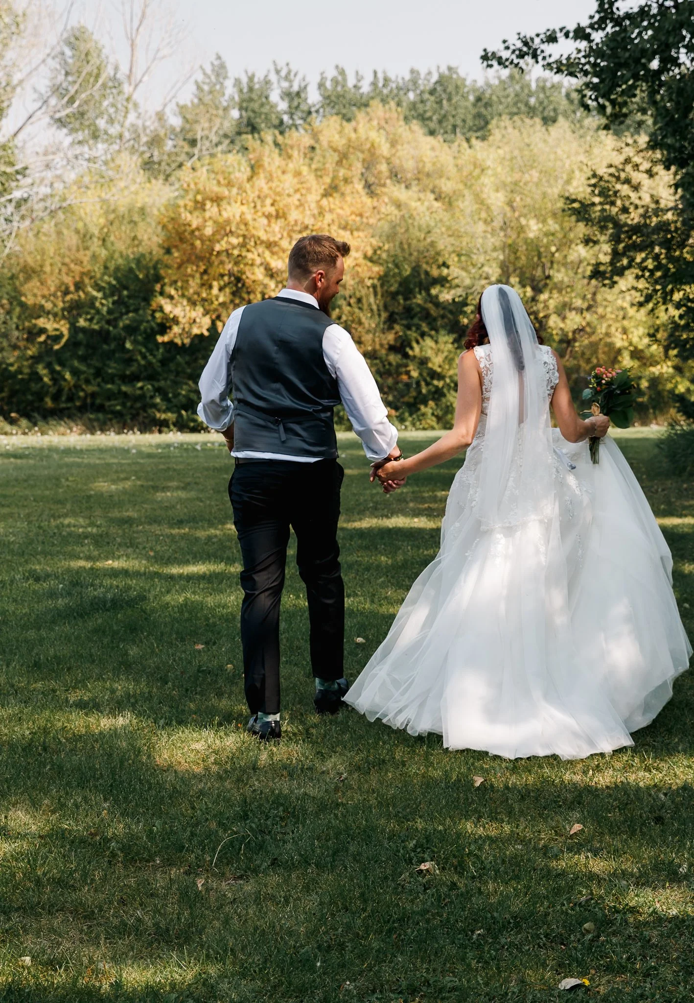 A bride and groom holding hands in a park with trees in the background during daytime.