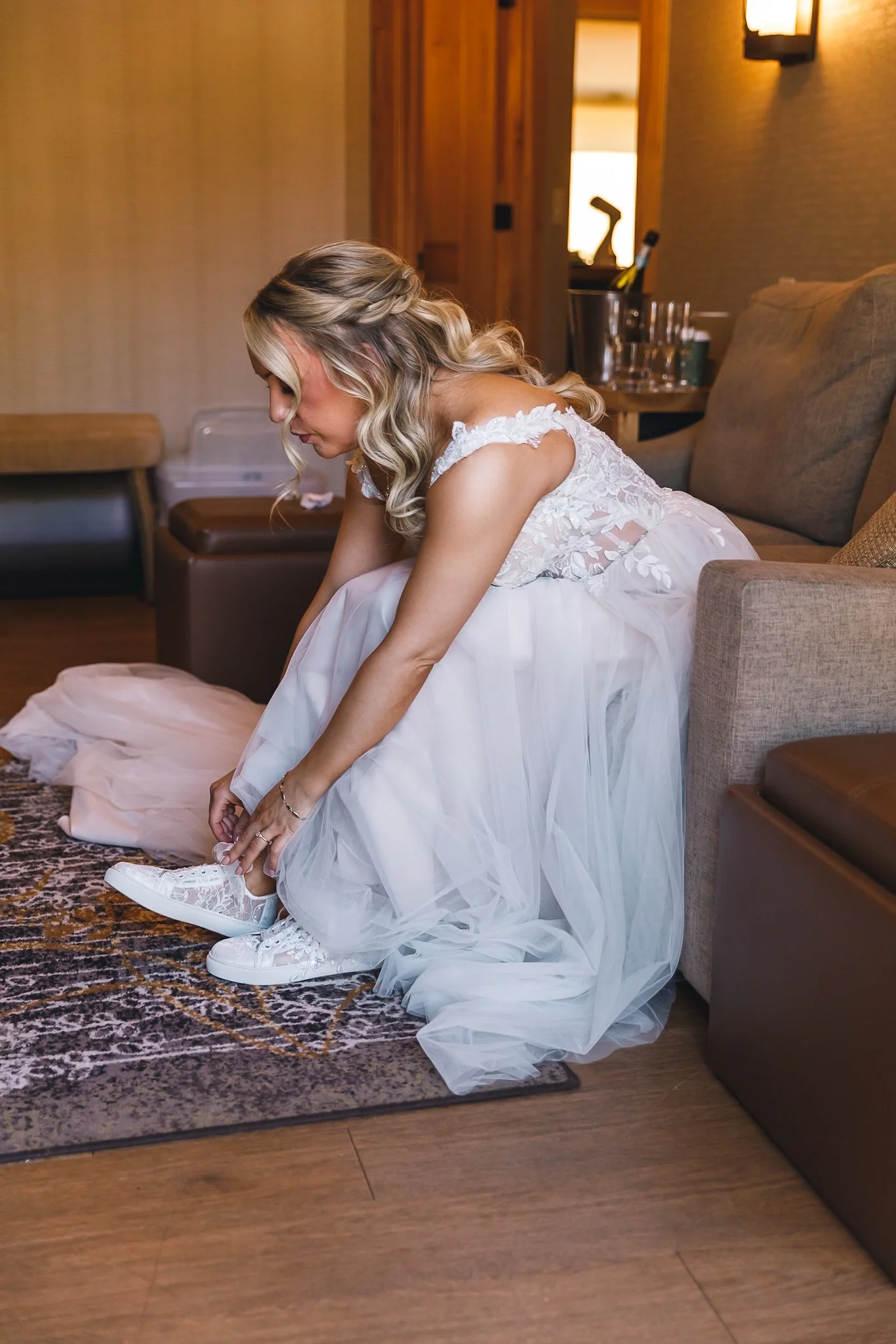 A bride in a wedding dress tying her shoelaces in a hotel room.