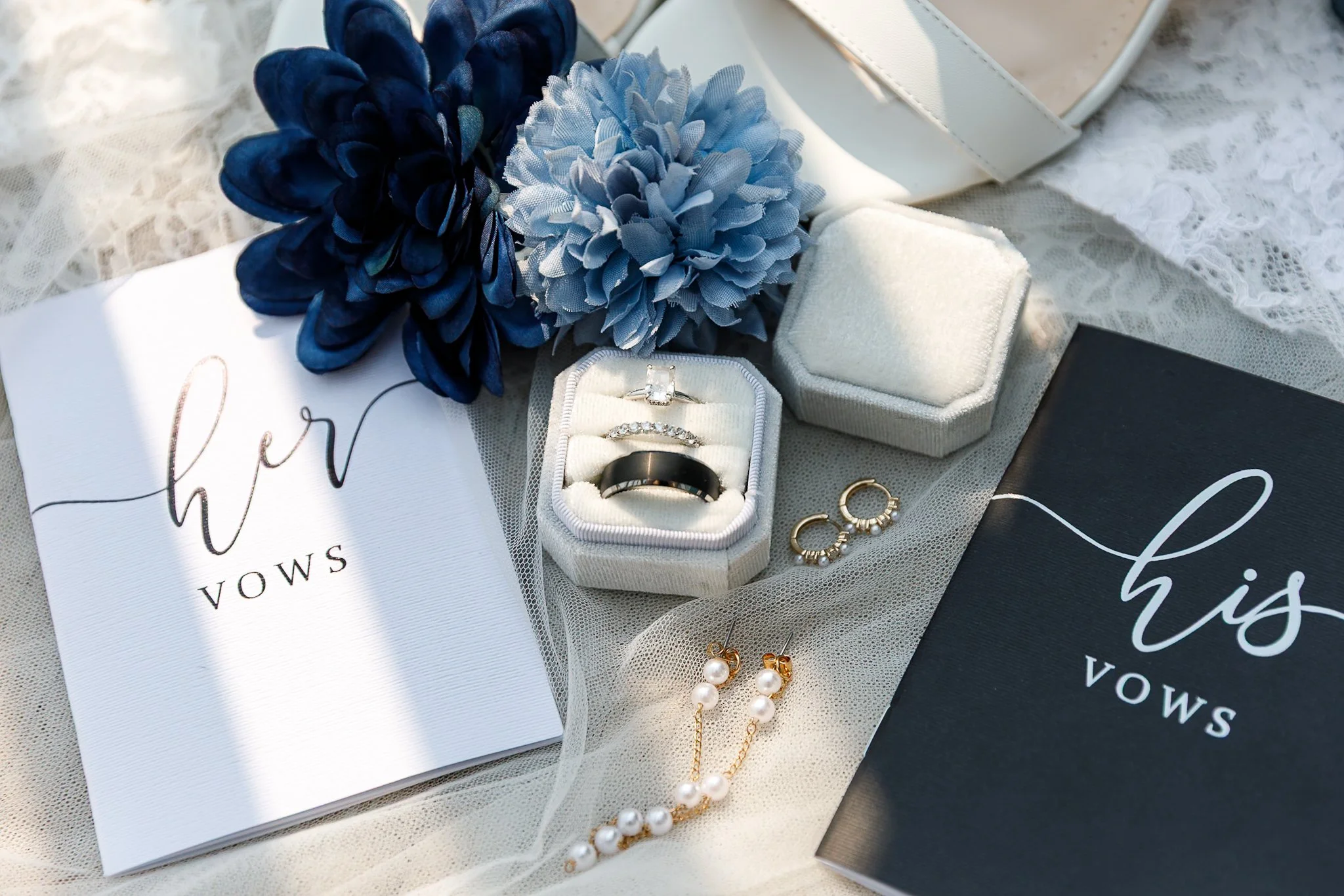 A jewelry box with rings, earrings, and a necklace, accompanied by blue and navy fake flowers and welcome gift boxes.