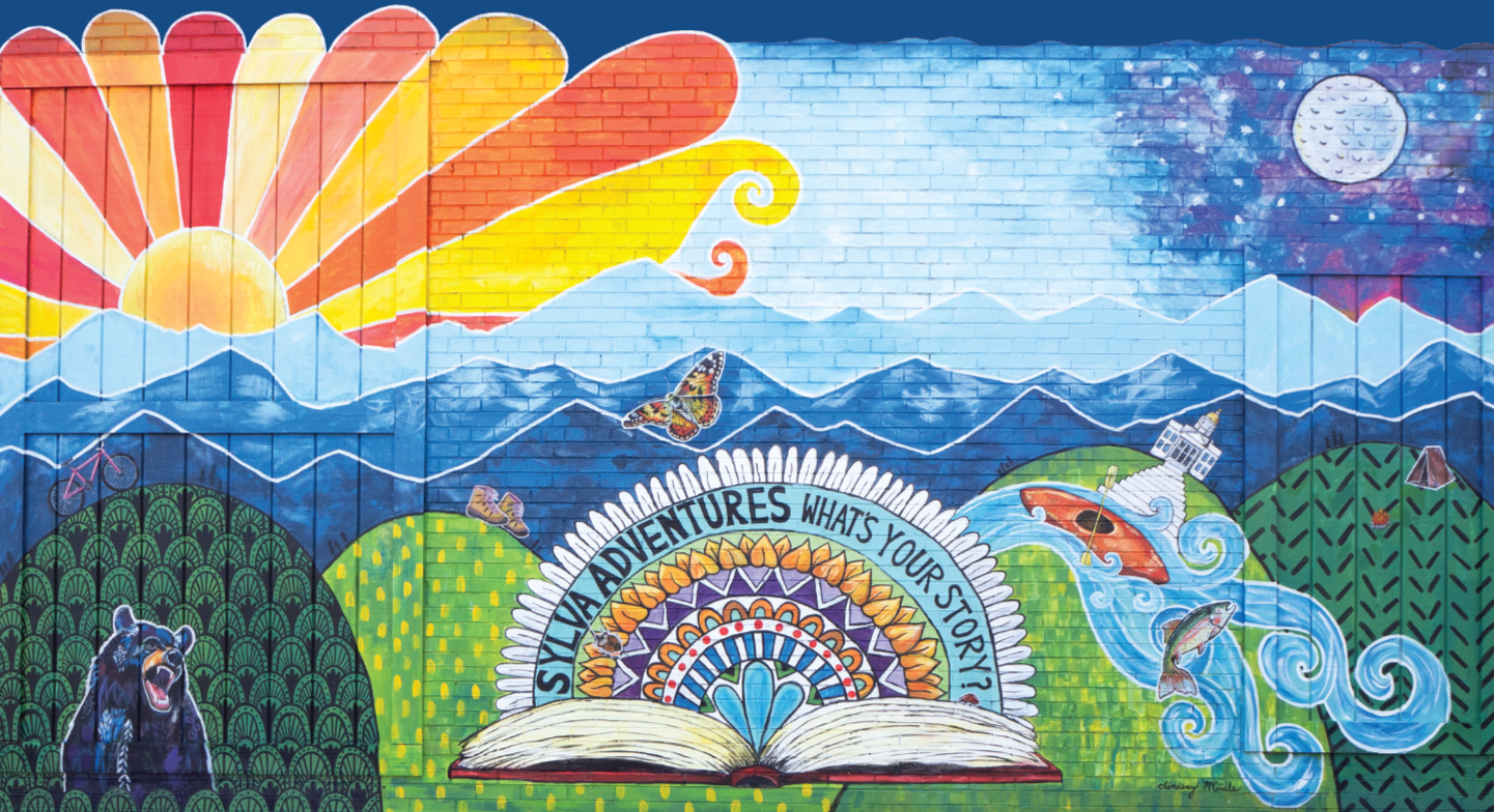 Colorful mural of mountains, sun, moon, fish, waterfall, bear, butterflies, and an open book with the phrase "Silvia Adventures, What's Your Story?"