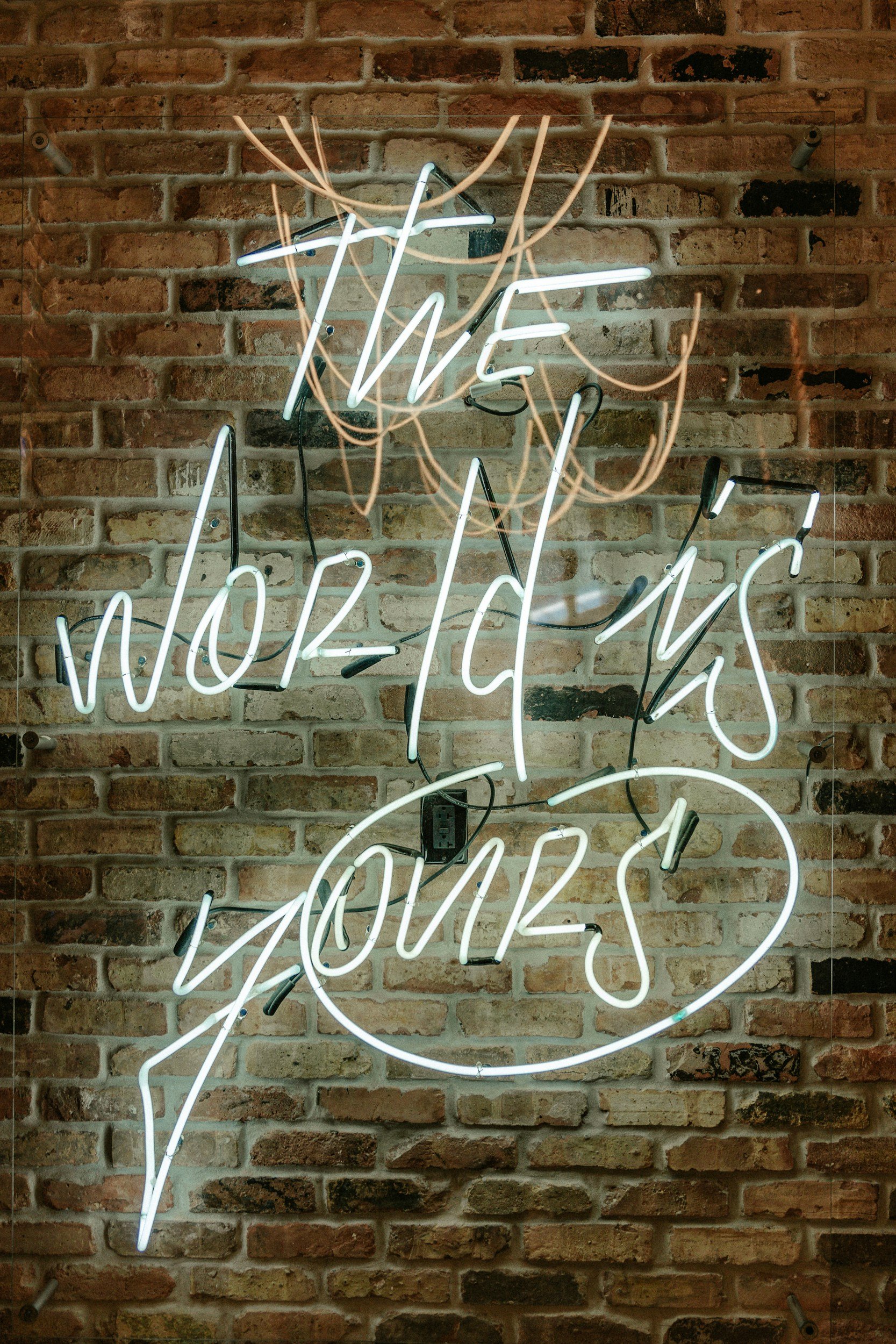 Neon sign with cursive writing that says 'We' and 'Lovers' on a brick wall background.