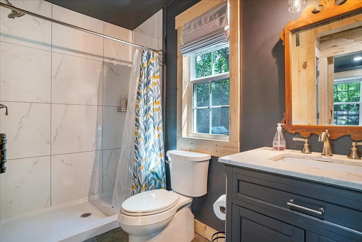 Bathroom with a window, a toilet, a vanity with a marble countertop, and a shower with marble tiles and a colorful curtain.