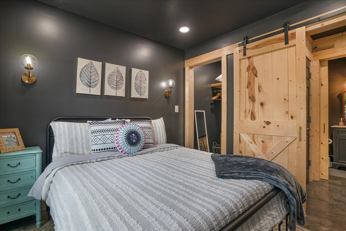 A bedroom with a dark gray accent wall, a bed with striped bedding and decorative pillows, a teal nightstand, and a wooden sliding barn door.