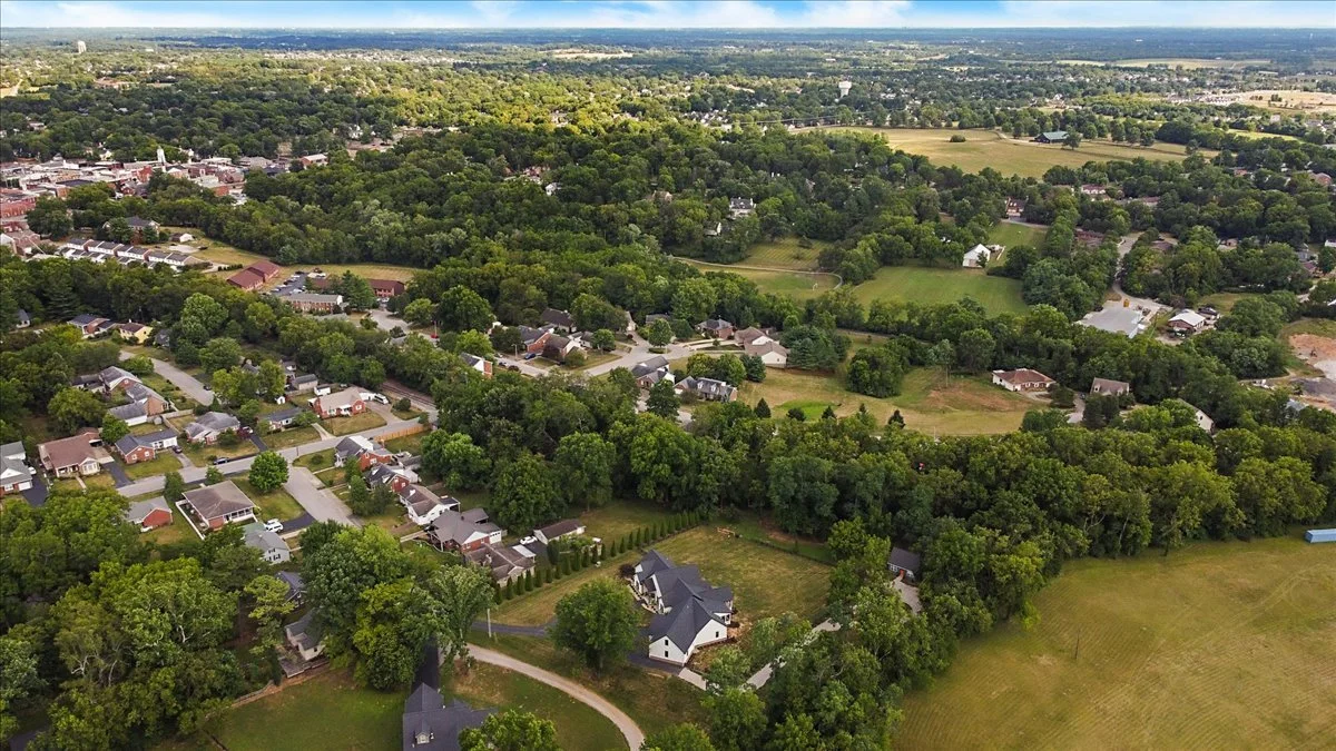 Aerial view of a suburban neighborhood with houses, trees, and open green spaces.