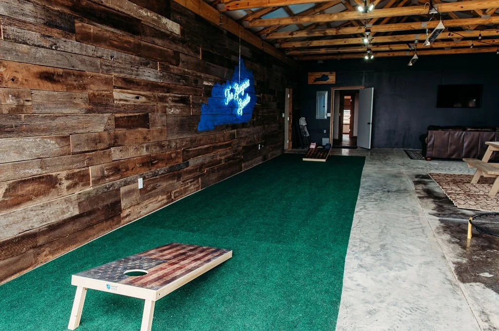 Indoor cornhole game setup with two wooden cornhole boards and a green artificial turf area.