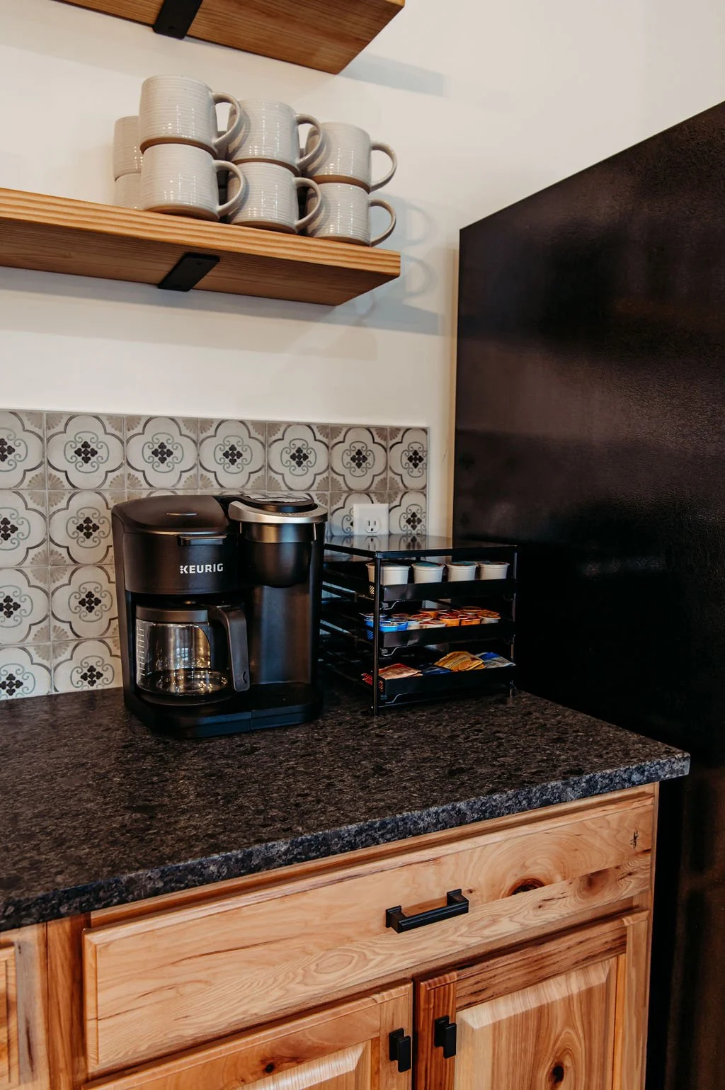 Coffee station with Keurig coffee maker, shelves with white mugs, and a countertop with coffee pods and cups.