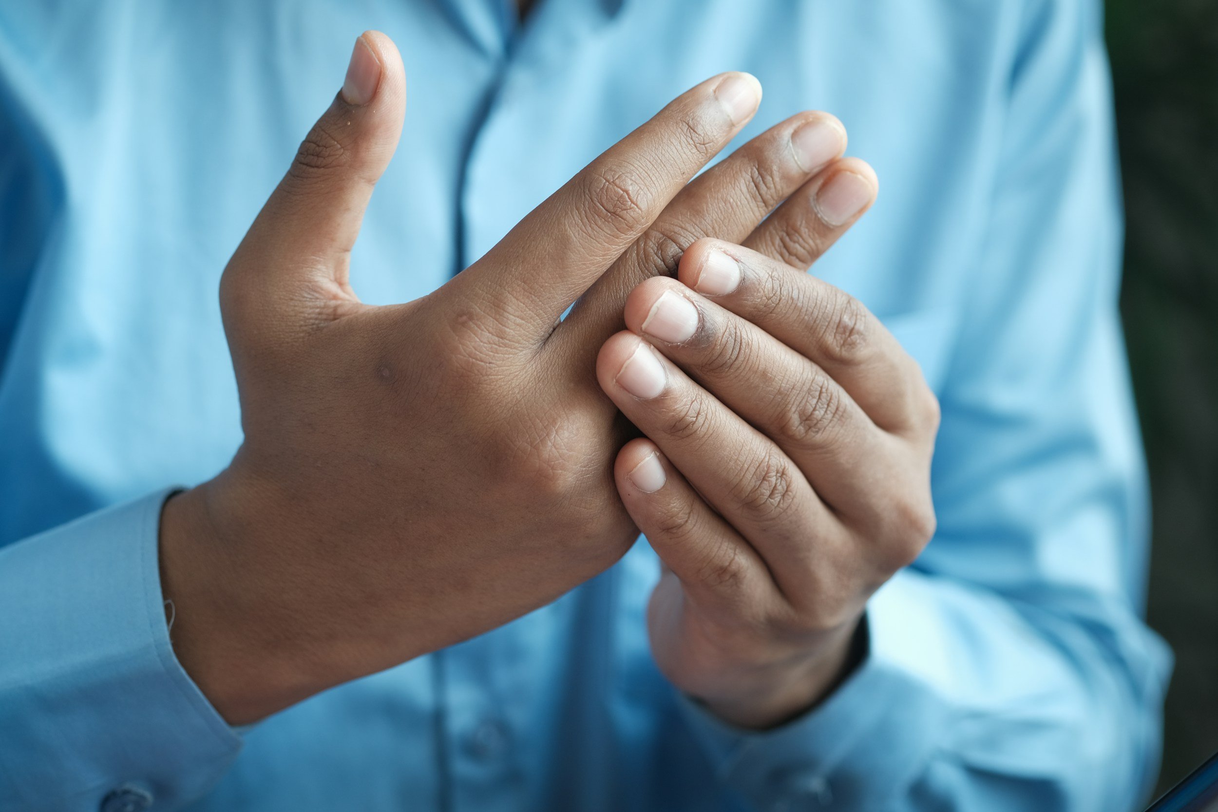 Close-up of a person's hands crossing over their chest, wearing a blue shirt.