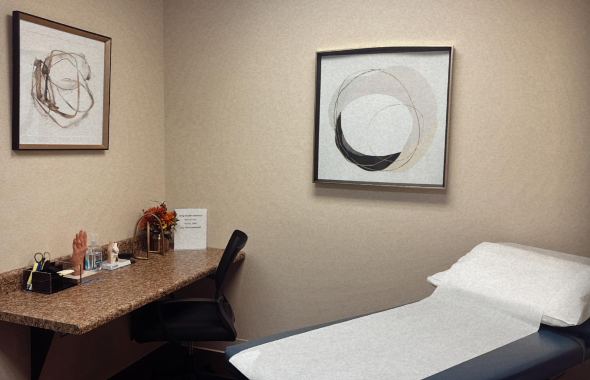 Hospital room with a bed, desk, and artwork on beige walls.