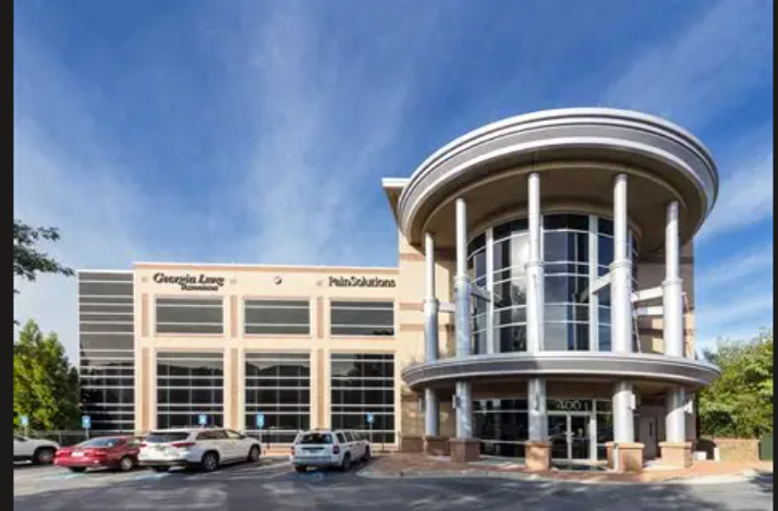 Exterior of a modern office building with a curved glass facade and parking lot in front.