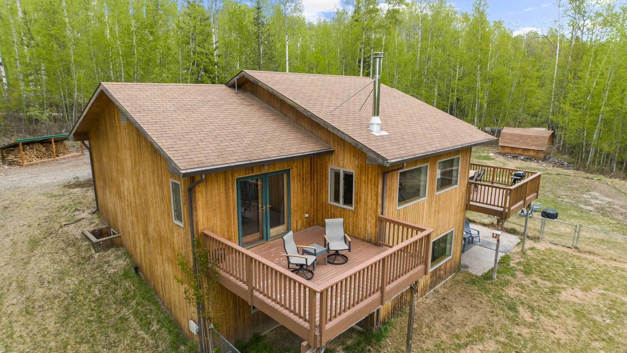 A wooden house with a deck and outdoor furniture, surrounded by trees and greenery.