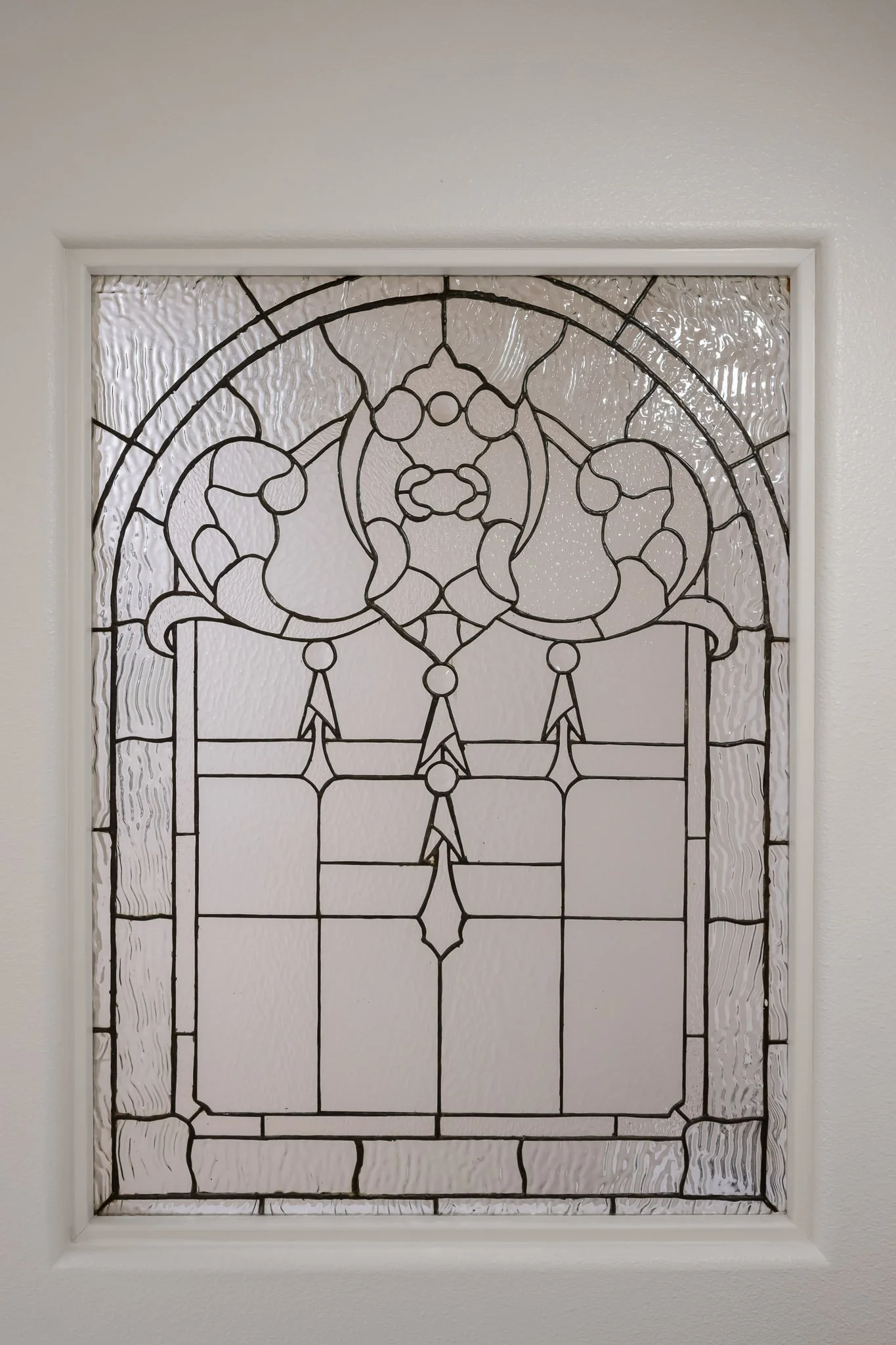 Decorative stained glass window with intricate black metal design framed in white, set in a white wall.