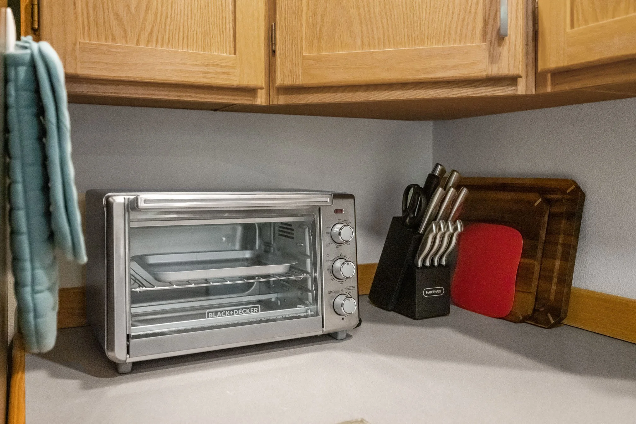 Kitchen counter with a small oven, a knife block with knives, and a red chair.