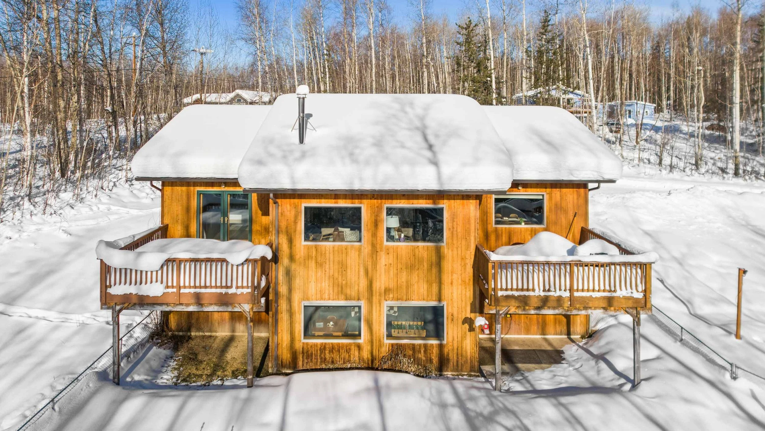 Snow-covered wooden house with balconies, surrounded by snow and trees.