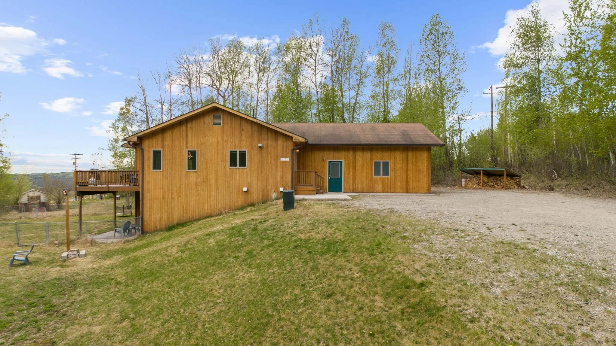 A wooden house with a blue door, surrounded by trees and a grassy yard, with a gravel area in front.