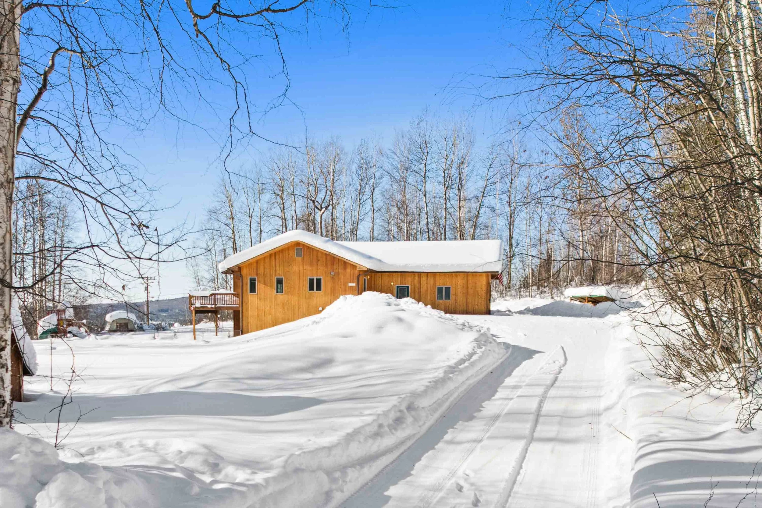 A wooden house with a snow-covered roof in a snowy landscape with trees and a clear blue sky.