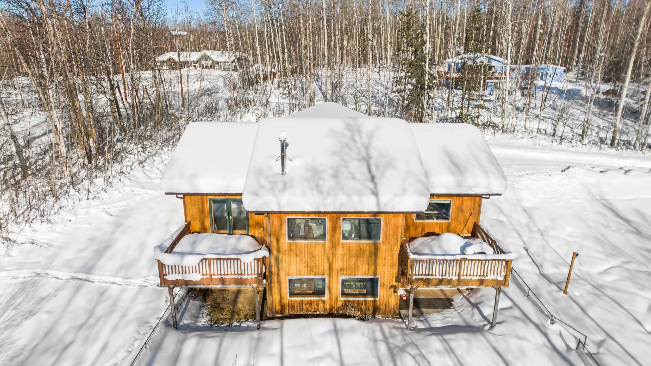 Aerial view of a two-story wooden house with a snow-covered roof, surrounded by snow and trees in a residential area.