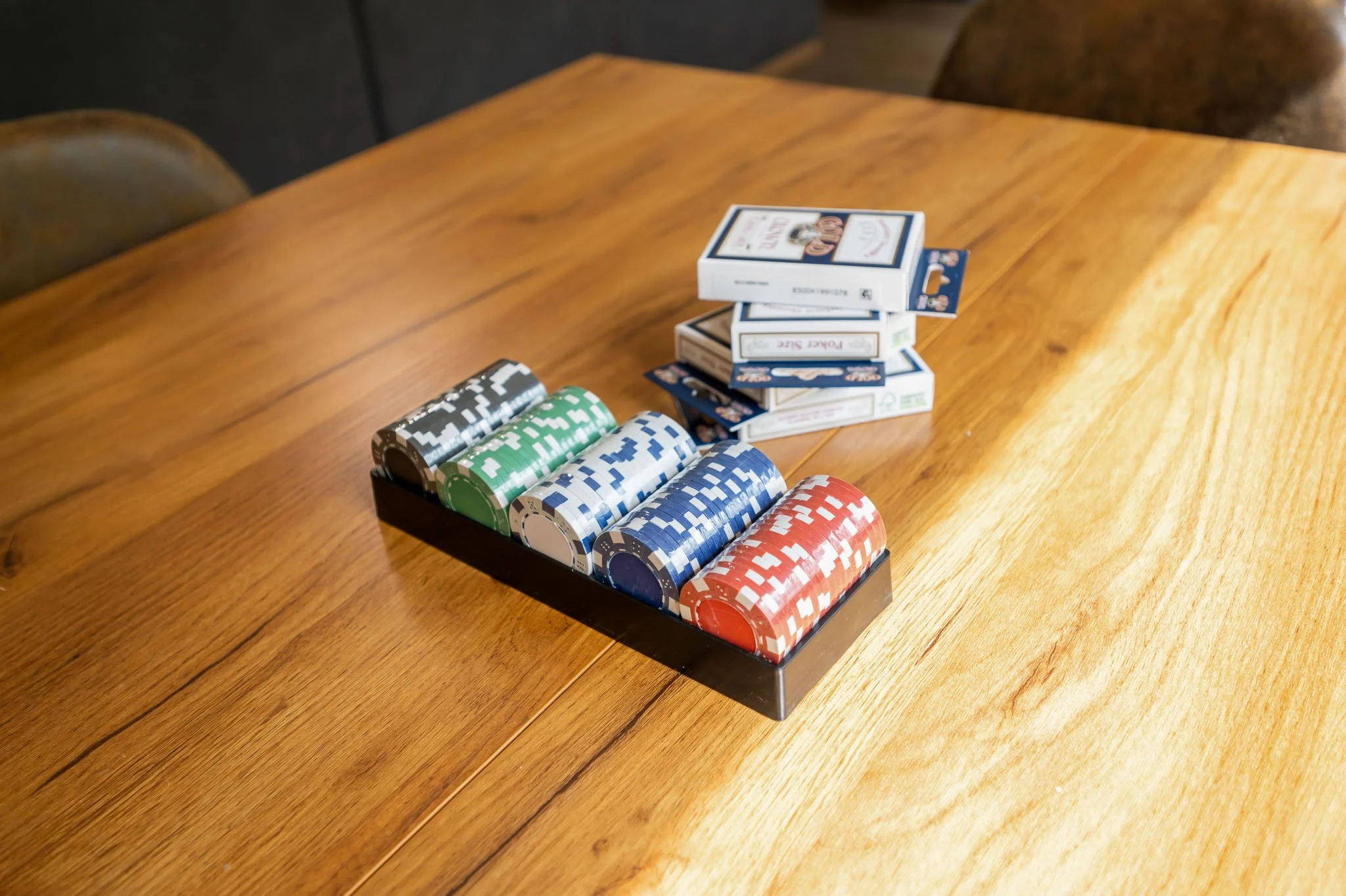 Stack of poker chips in various colors on a black tray on a wooden table.