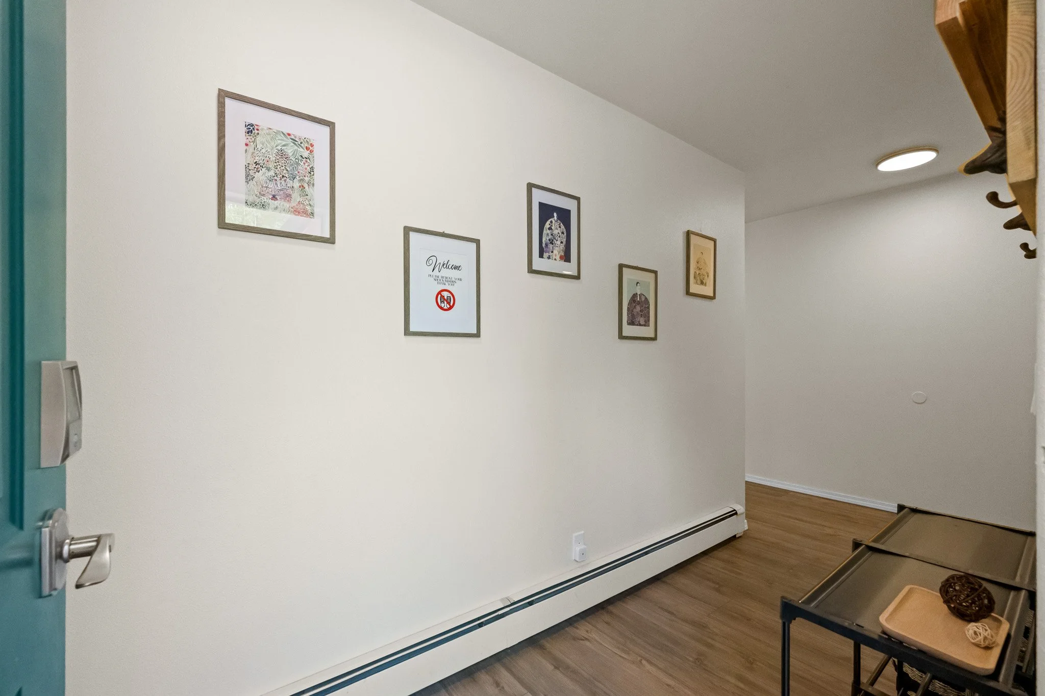 Empty wall with framed artwork in a room, with part of a table holding decorative items and a wooden shoe rack visible.