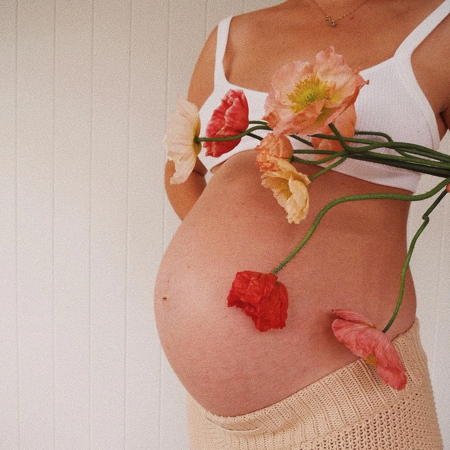Close-up of a person's lower back and buttocks, wearing white lace underwear, with a bouquet of colorful flowers resting on the skin.
