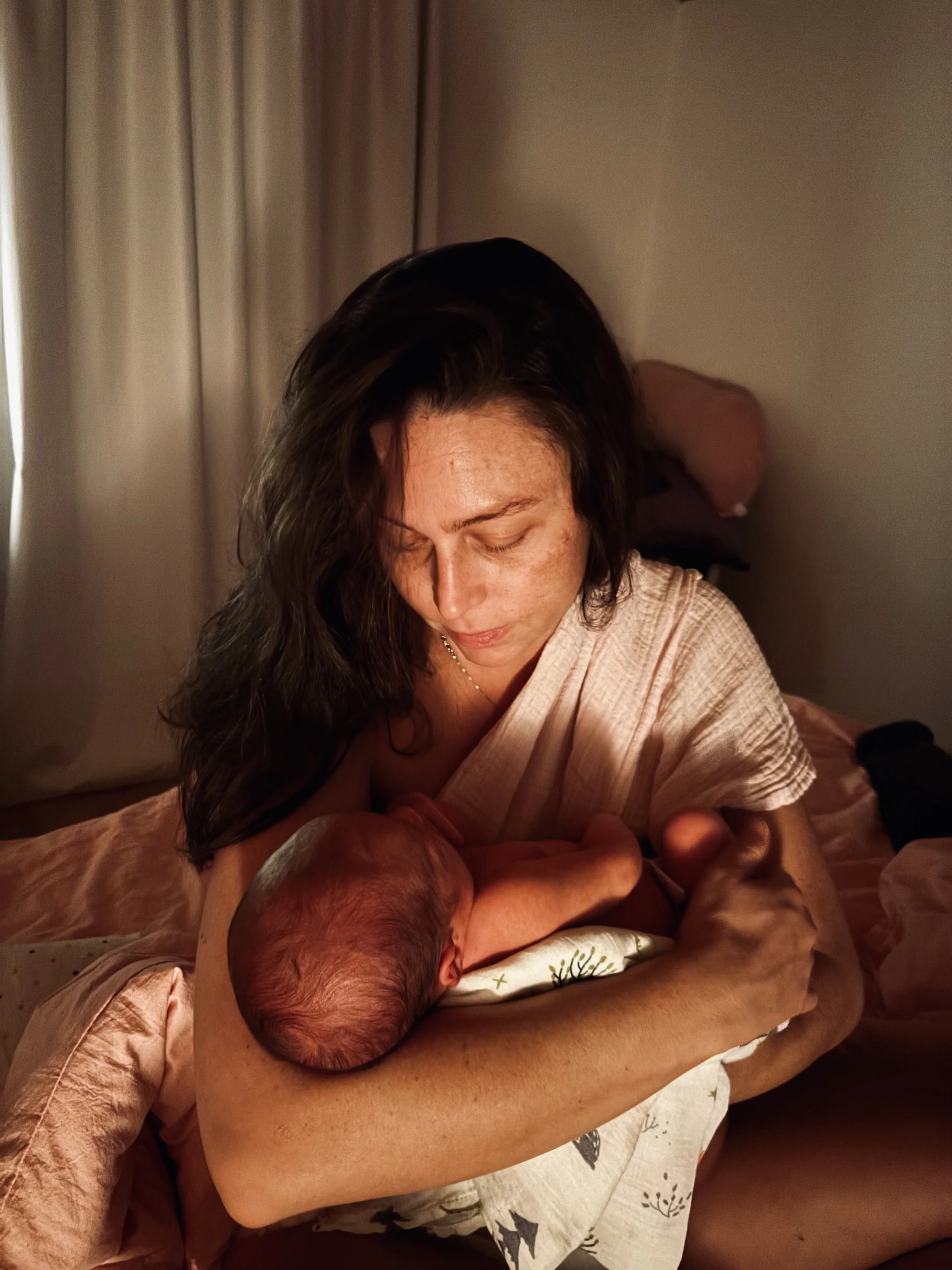 A woman with dark hair holding a newborn baby in her arms at night, in a warmly lit room.