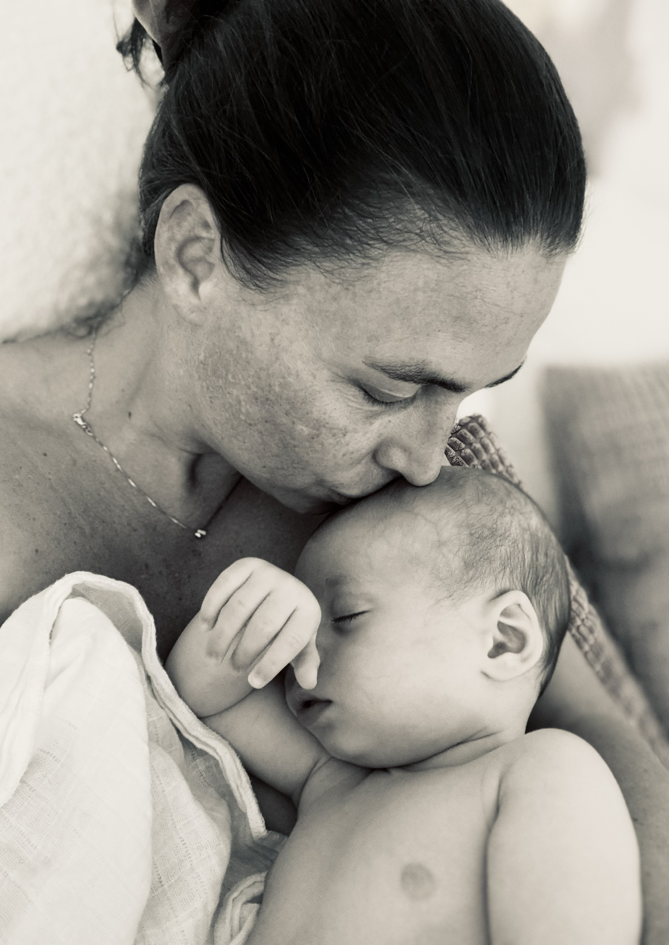 A black and white photo of a woman with dark hair holding a sleeping baby close to her face.