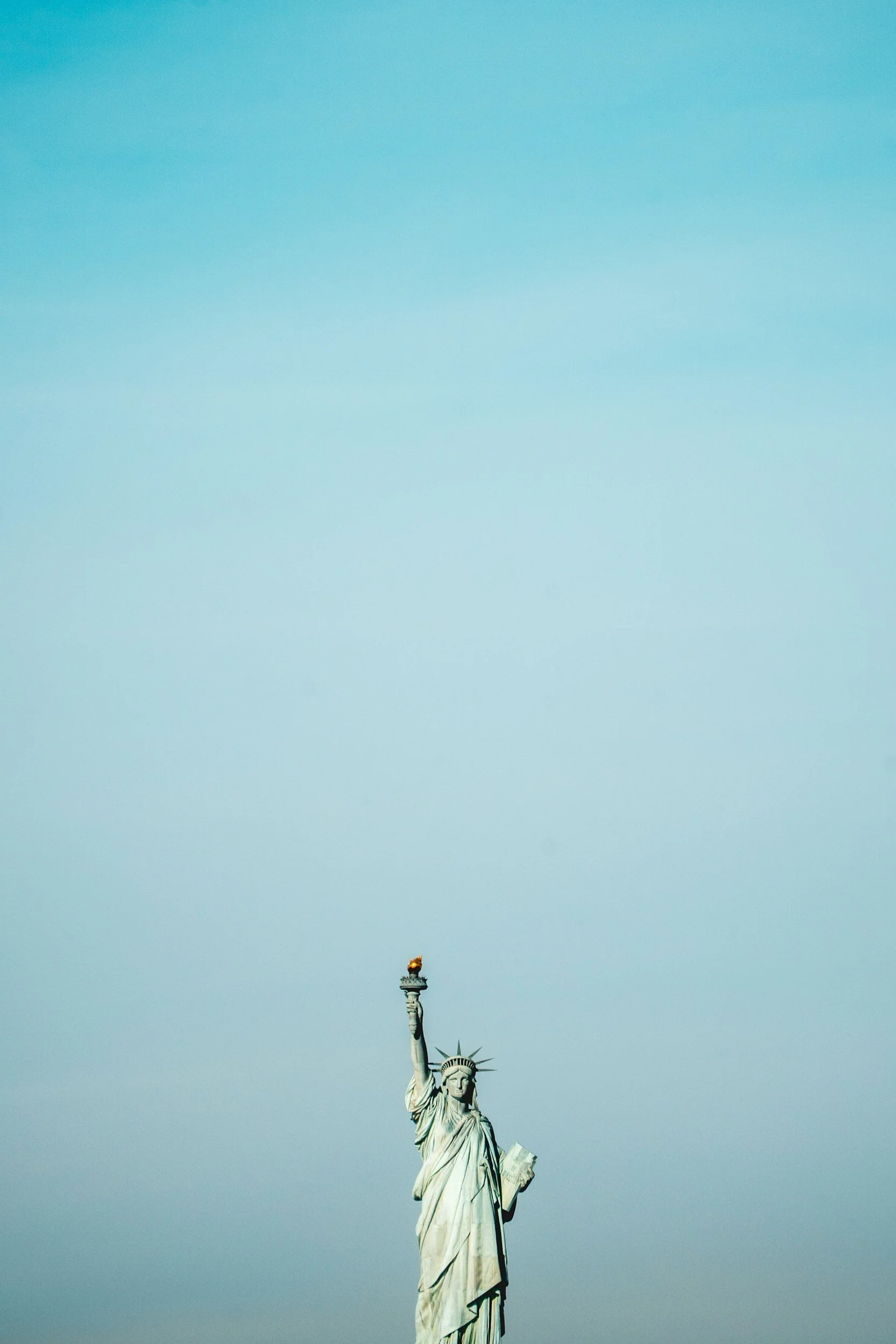 Statue of Liberty with a flag on top, set against a clear blue sky.