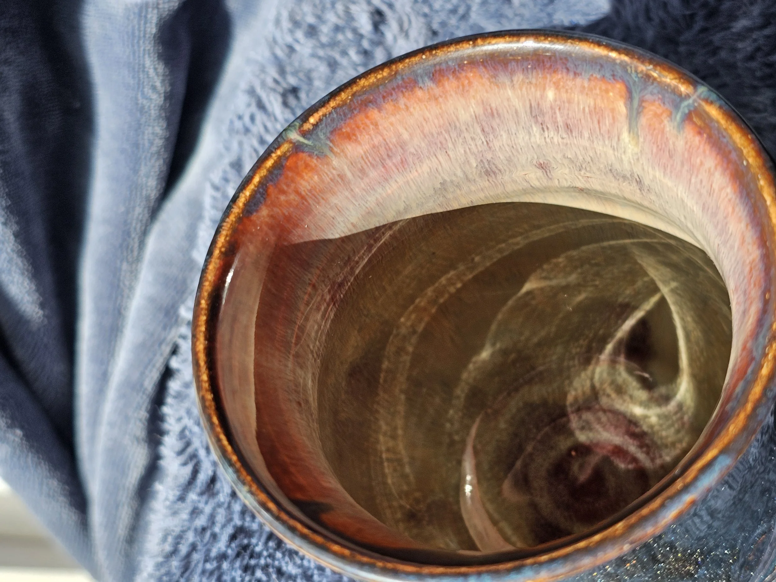 Close-up view of the inside of a ceramic cup with a glossy finish, showing a gradient of brown and reddish tones, placed on a textured surface.