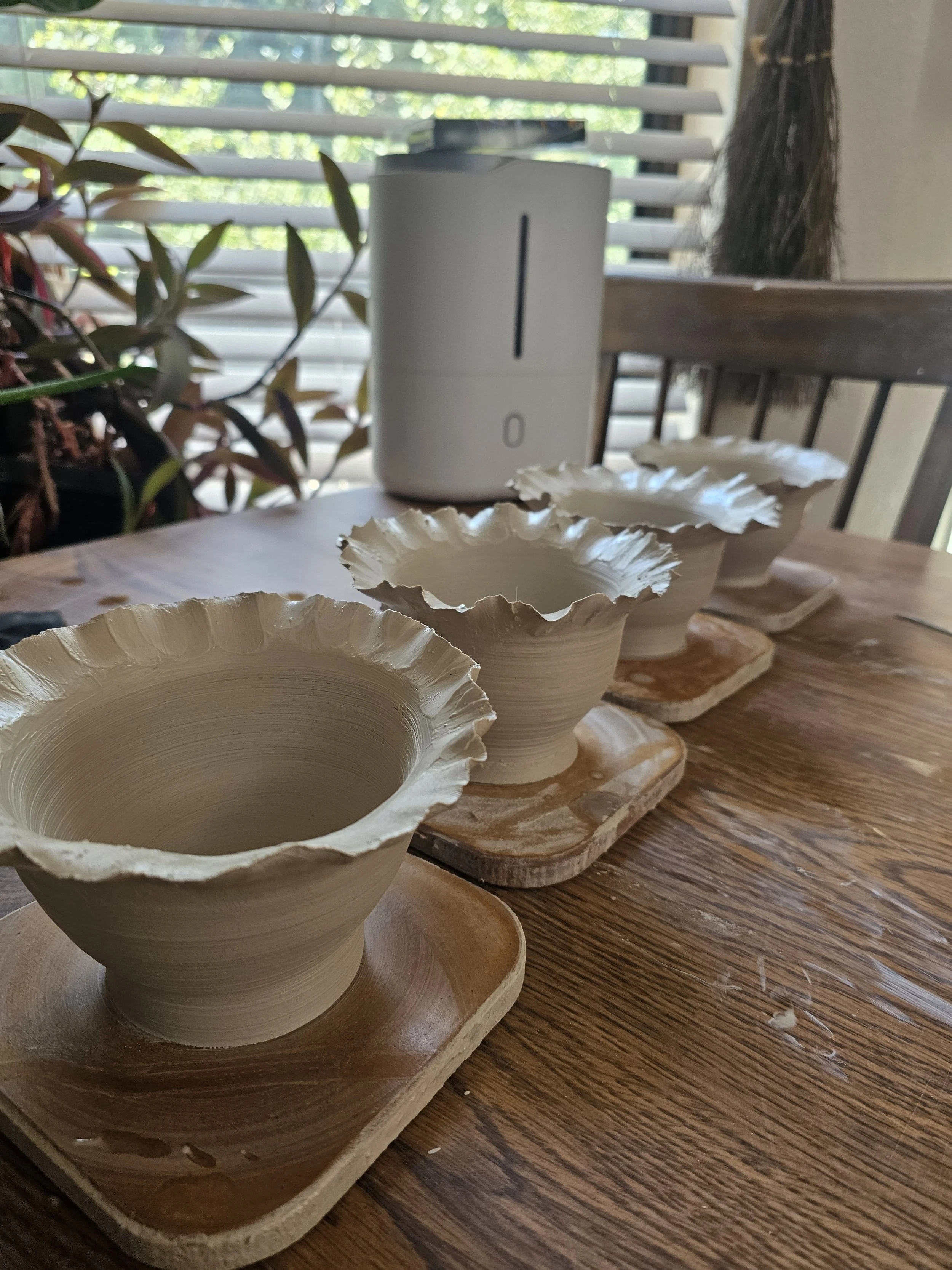 Four cream colored ceramic bowls with ruffled edges placed on wooden trays on a wooden table. 