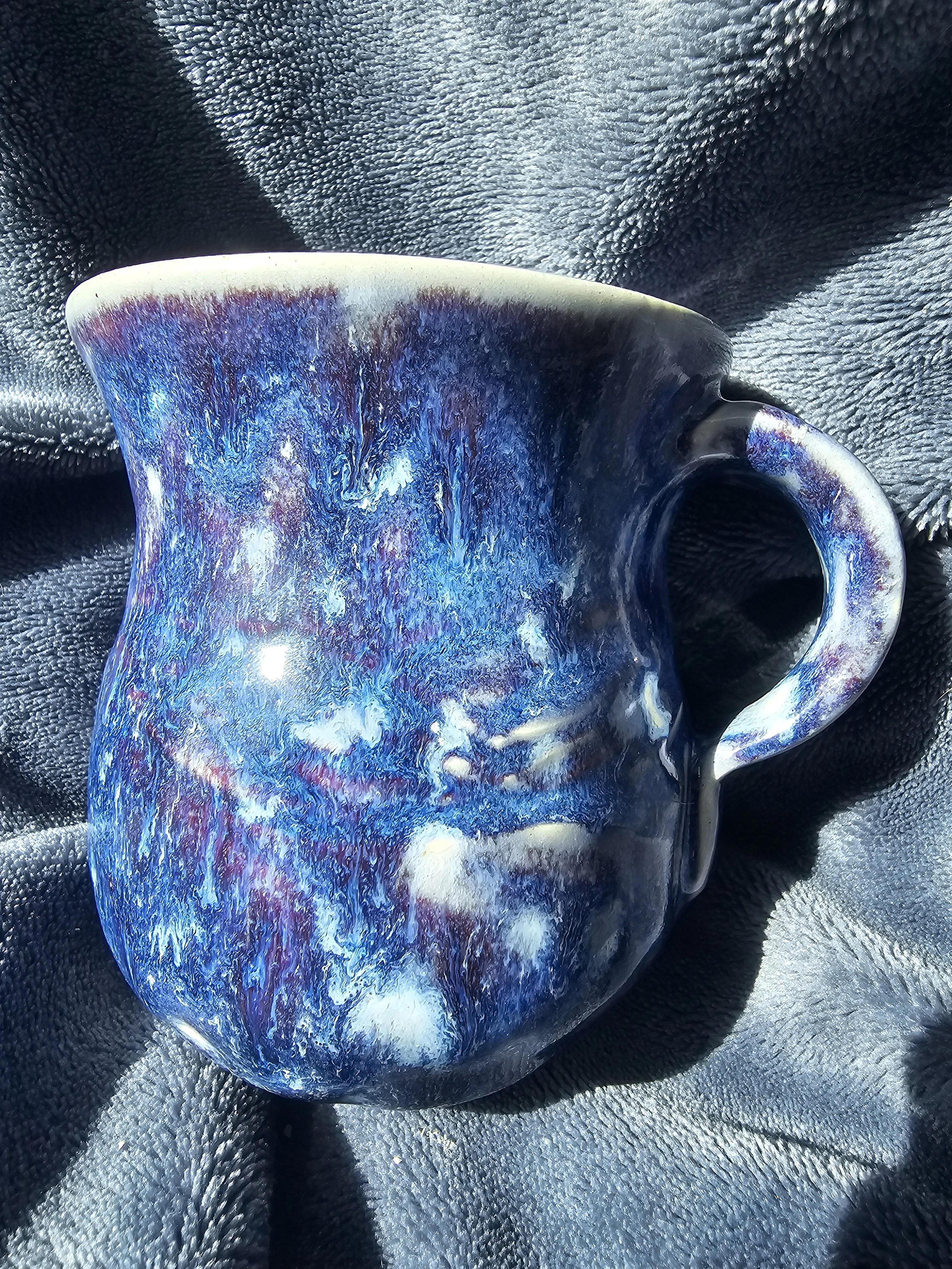 Close-up of a colorful glass mug with blue, purple, and white patterns, resting on a textured black and gray surface.
