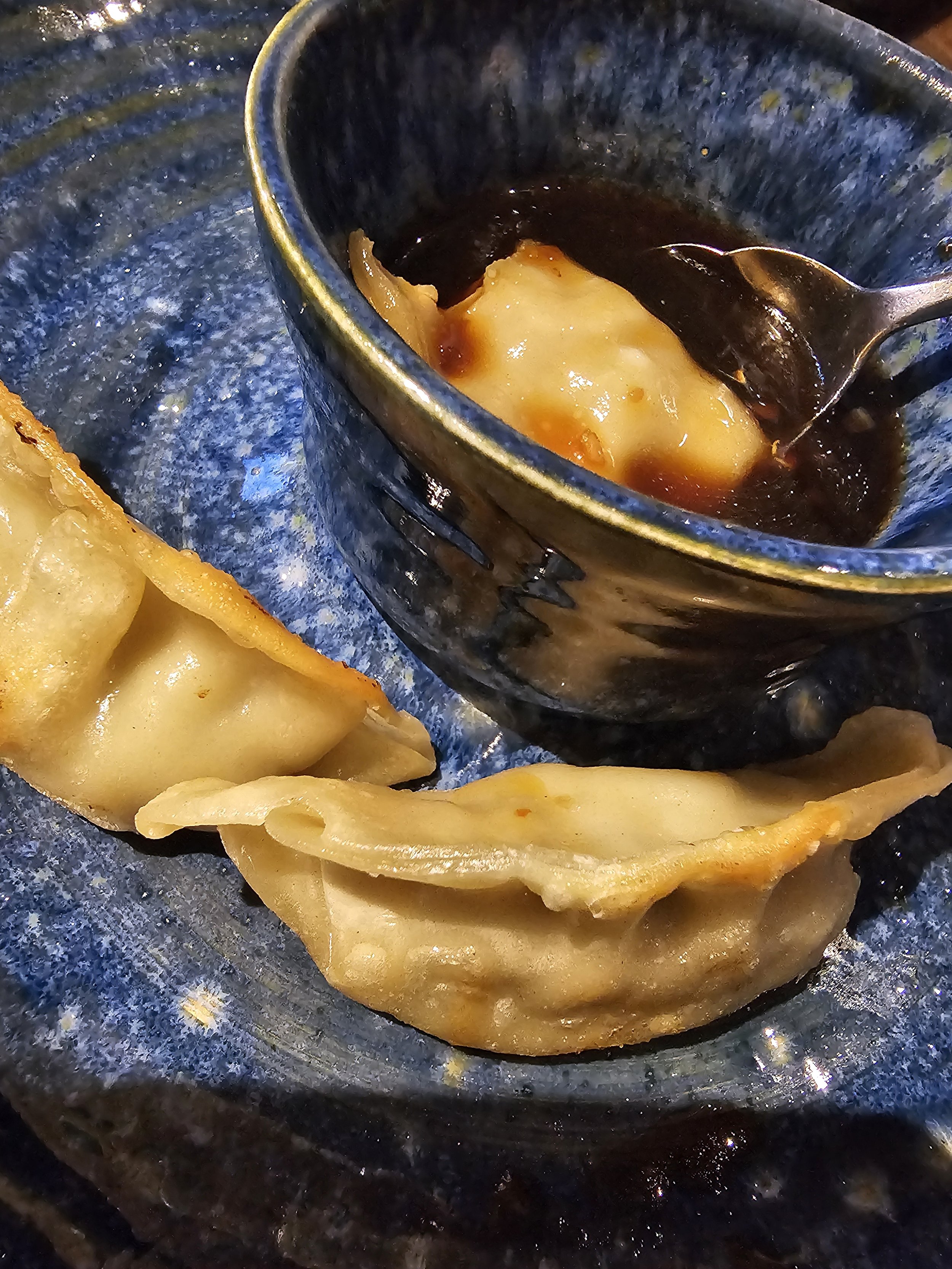 Fried dumplings with a side of dipping sauce in a blue bowl. The dumplings are golden brown and appear crispy.