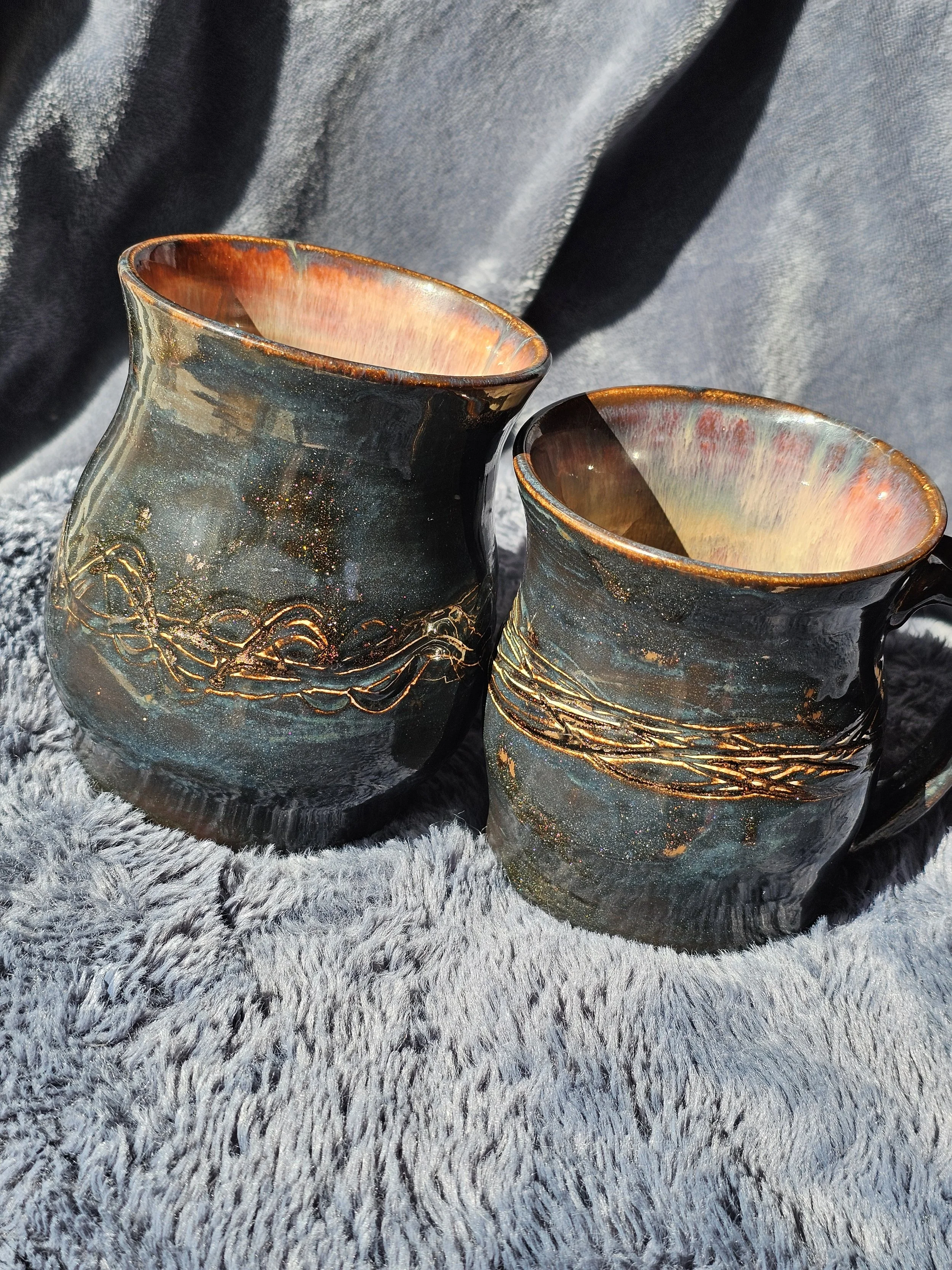Two handcrafted ceramic mugs with intricate golden patterns placed on a textured gray surface.