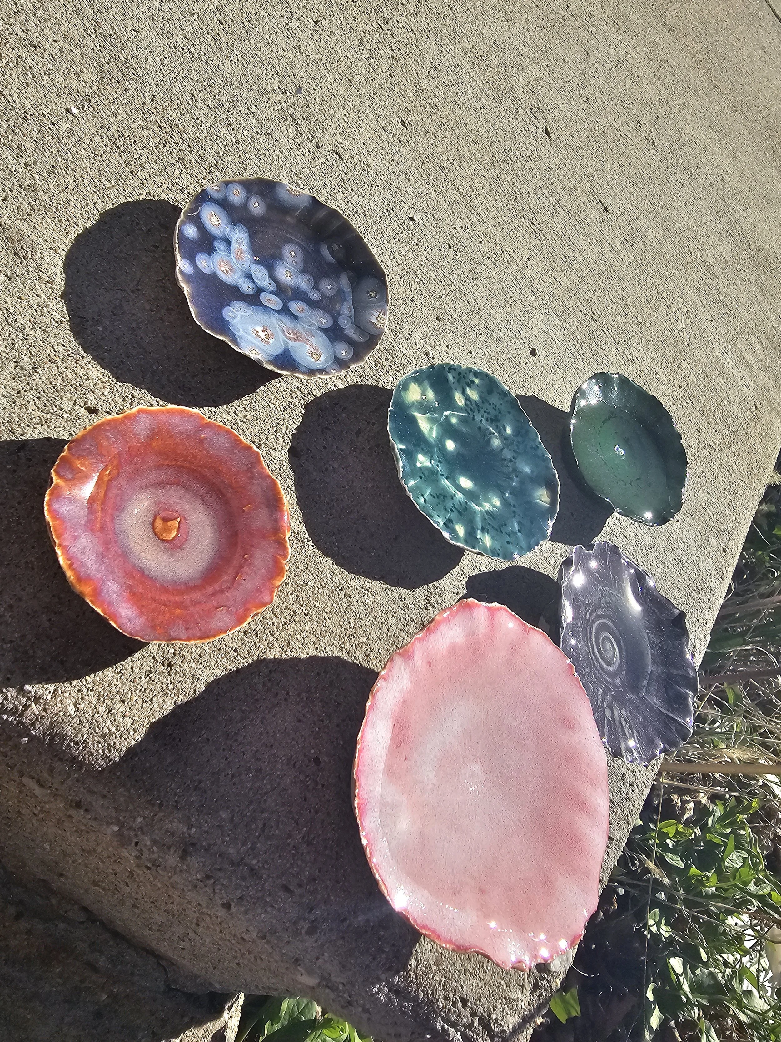 Colorful glass garden decorations shaped like slices of agate or geodes placed on a concrete surface with sunlight and shadows.