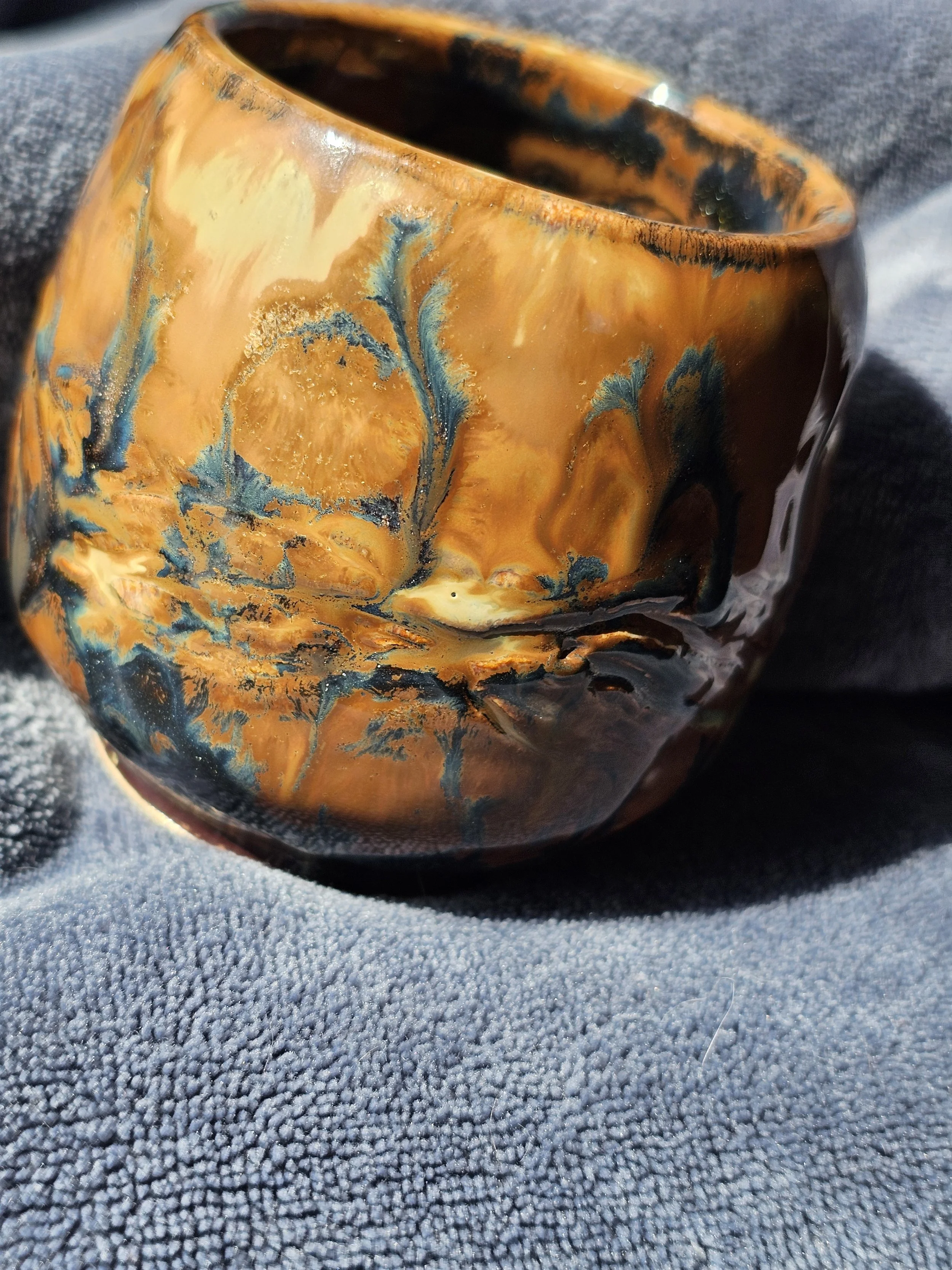 Close-up of a ceramic cup with orange, black, and blue swirling patterns resting on a textured gray  surface.