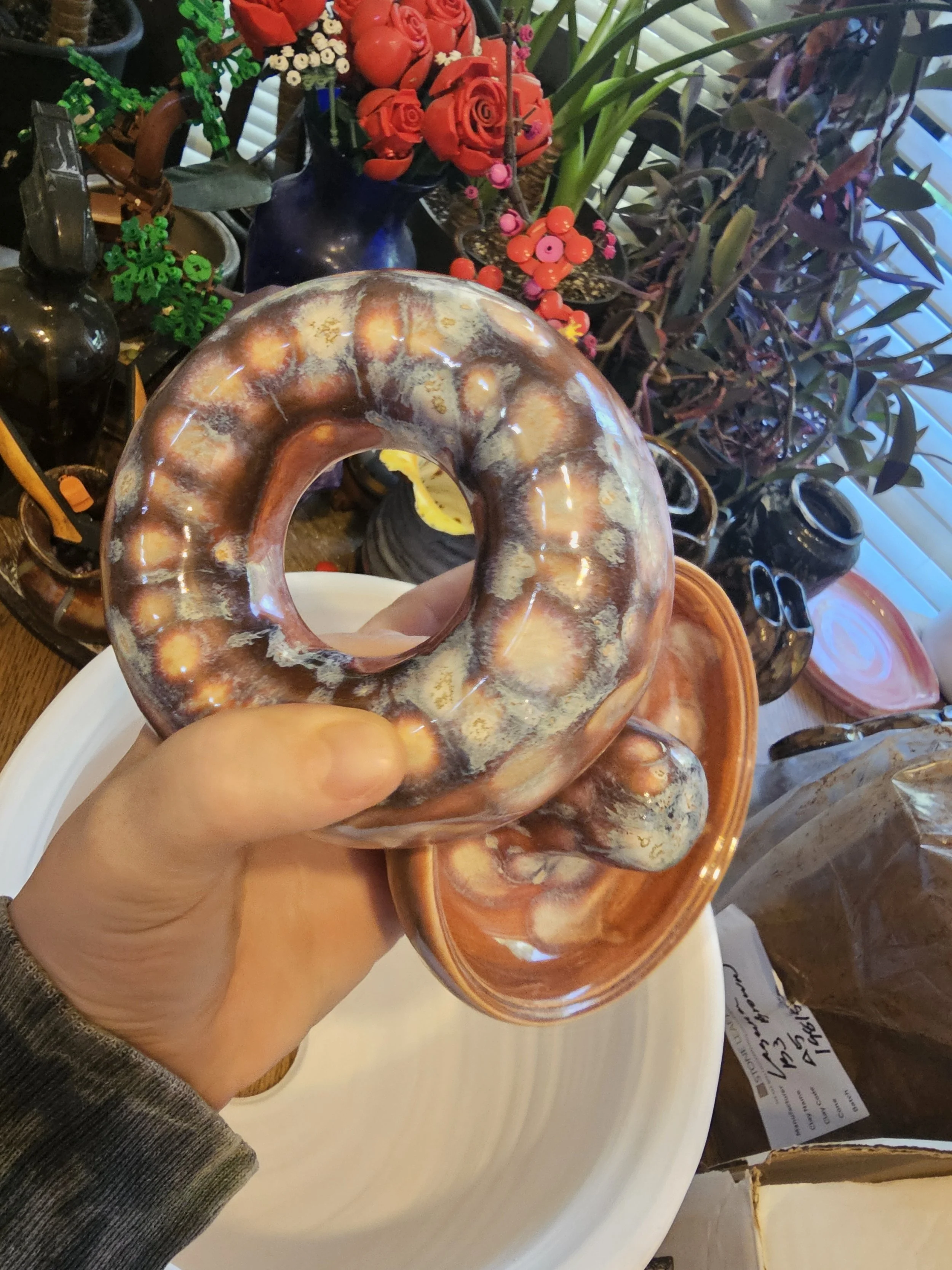 A hand holding a hole in the center ashtray, positioned over a white plate. In the background, there are various decorative items.