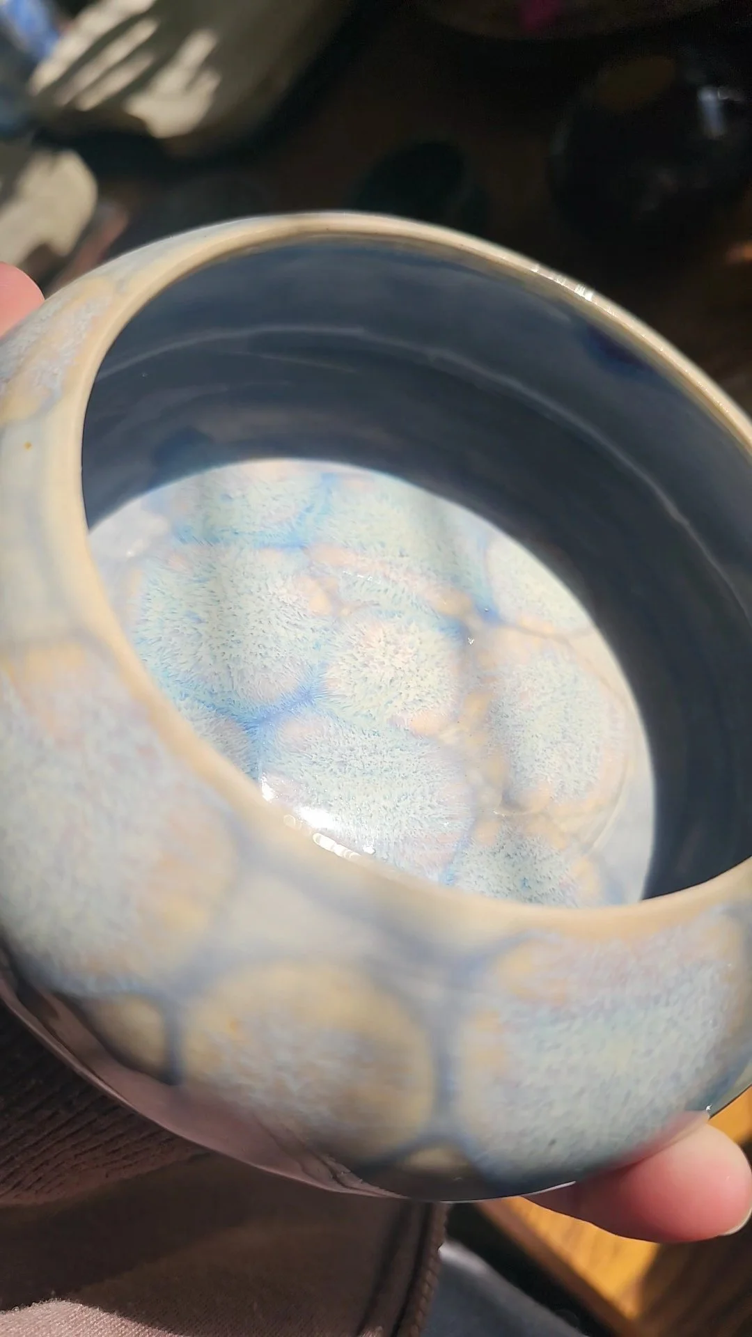 Close-up of a ceramic mug with a glossy, decorative glaze inside and a light-colored, textured exterior, held over a wooden surface.