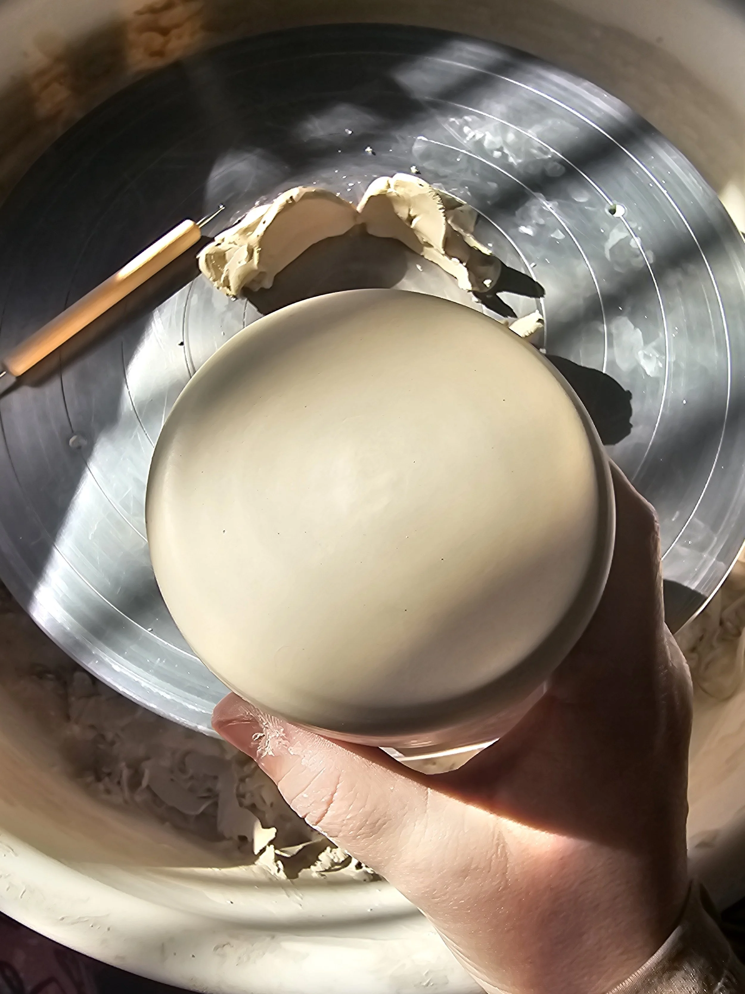 Person holding a round, pale-colored ceramic bowl with a creamy substance inside, over a mixing bowl with dough or batter.