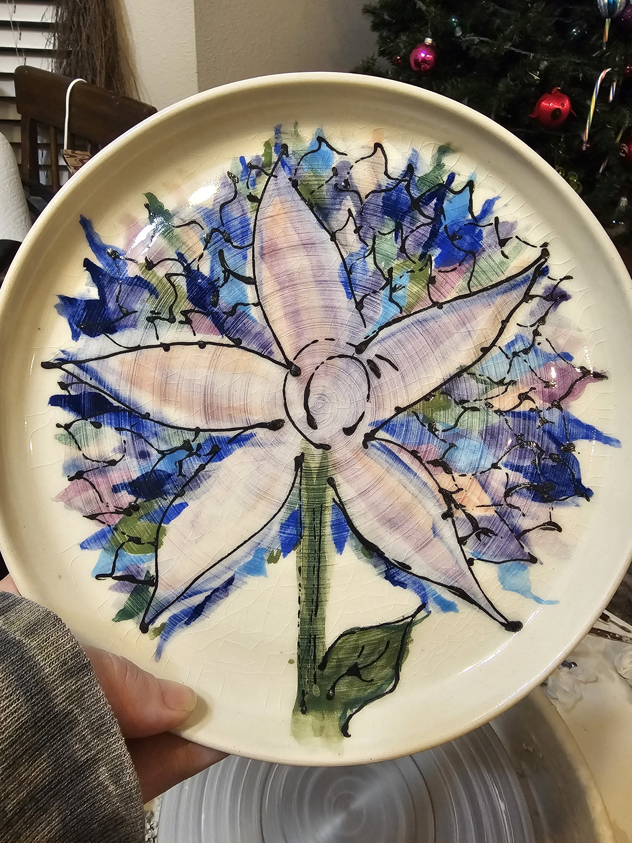 Decorative ceramic plate featuring a painted blue and purple butterfly with black outline and colorful background, being held by a person's hand.