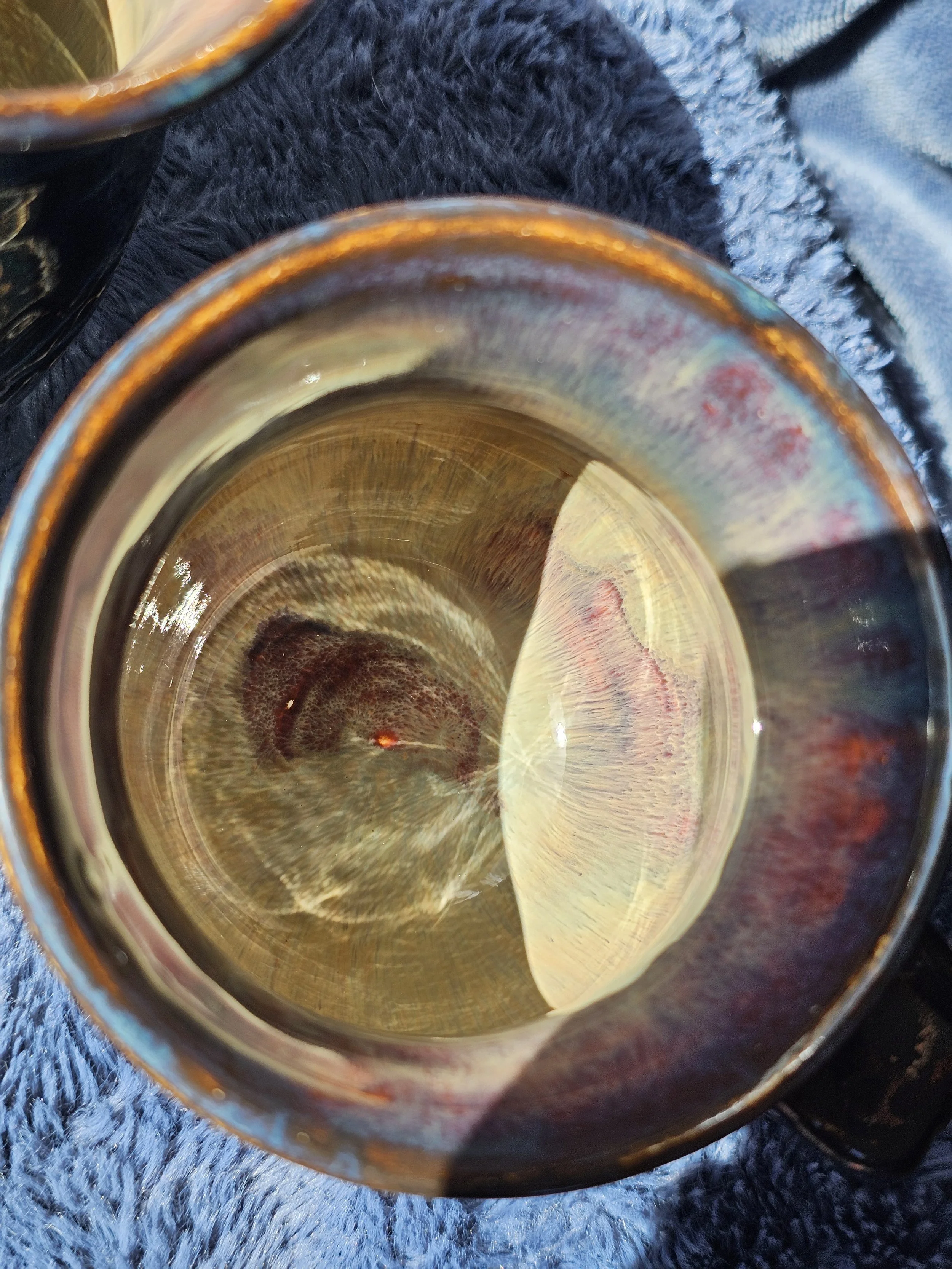 Close-up of a clear glass filled with a light-colored liquid, placed on a dark textured surface, with reflections and slight distortions visible in the glass.