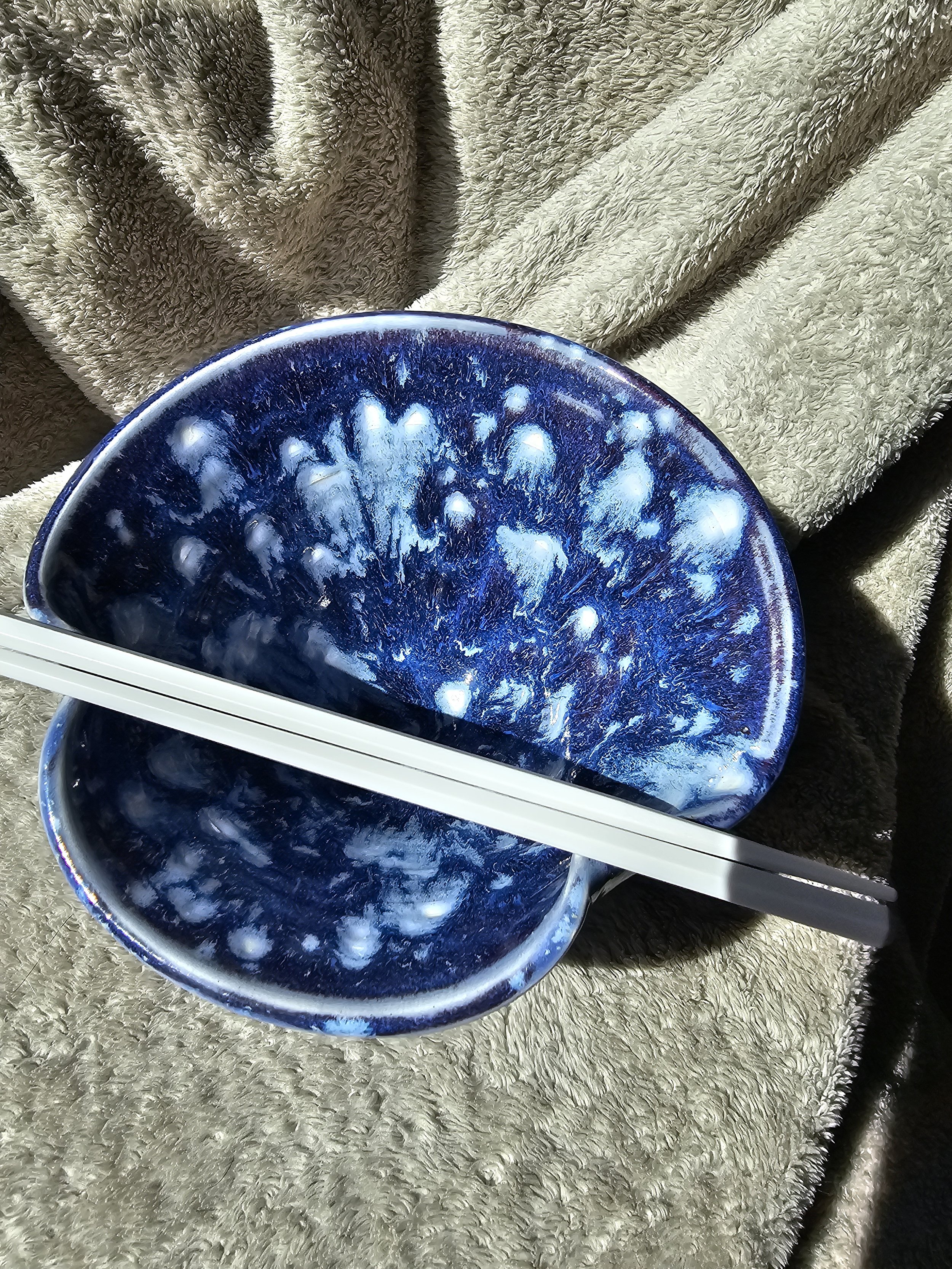 A round blue and white ceramic bowl with a textured glaze, with a pair of white chopsticks placed across the bowl.
