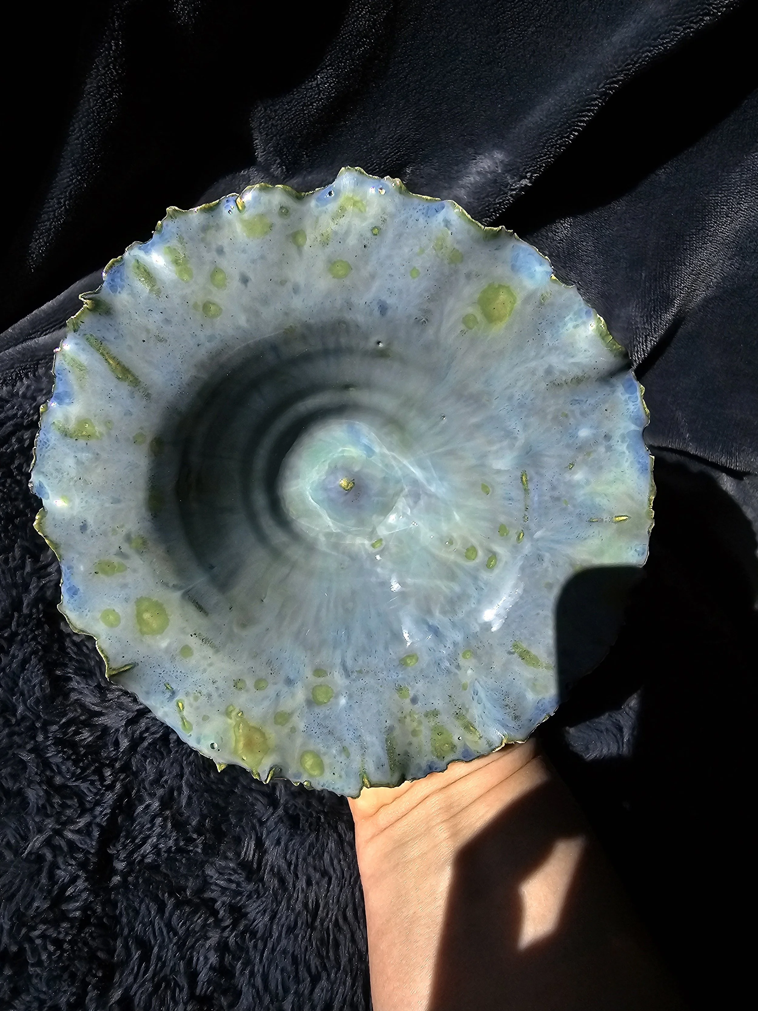 A person holding a polished, iridescent abalone shell looking ceramic bowl with a textured black fabric background.