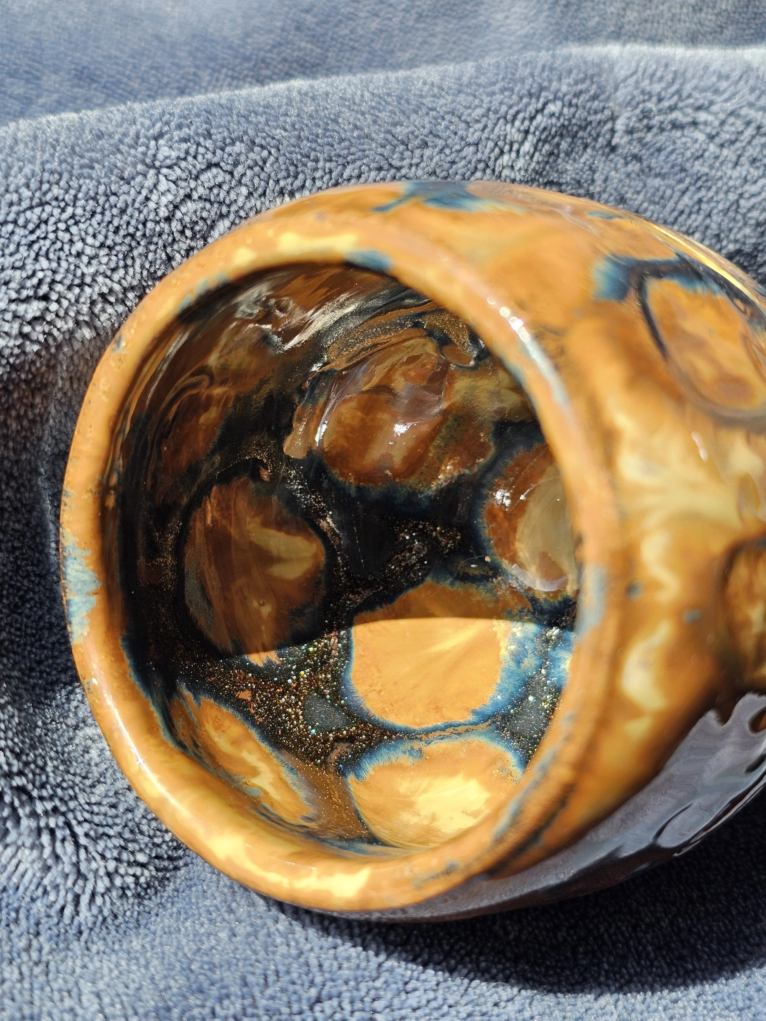 Close-up view of the inside of a ceramic mug with a marbled brown, blue, and orange glaze, resting on a dark textured surface.