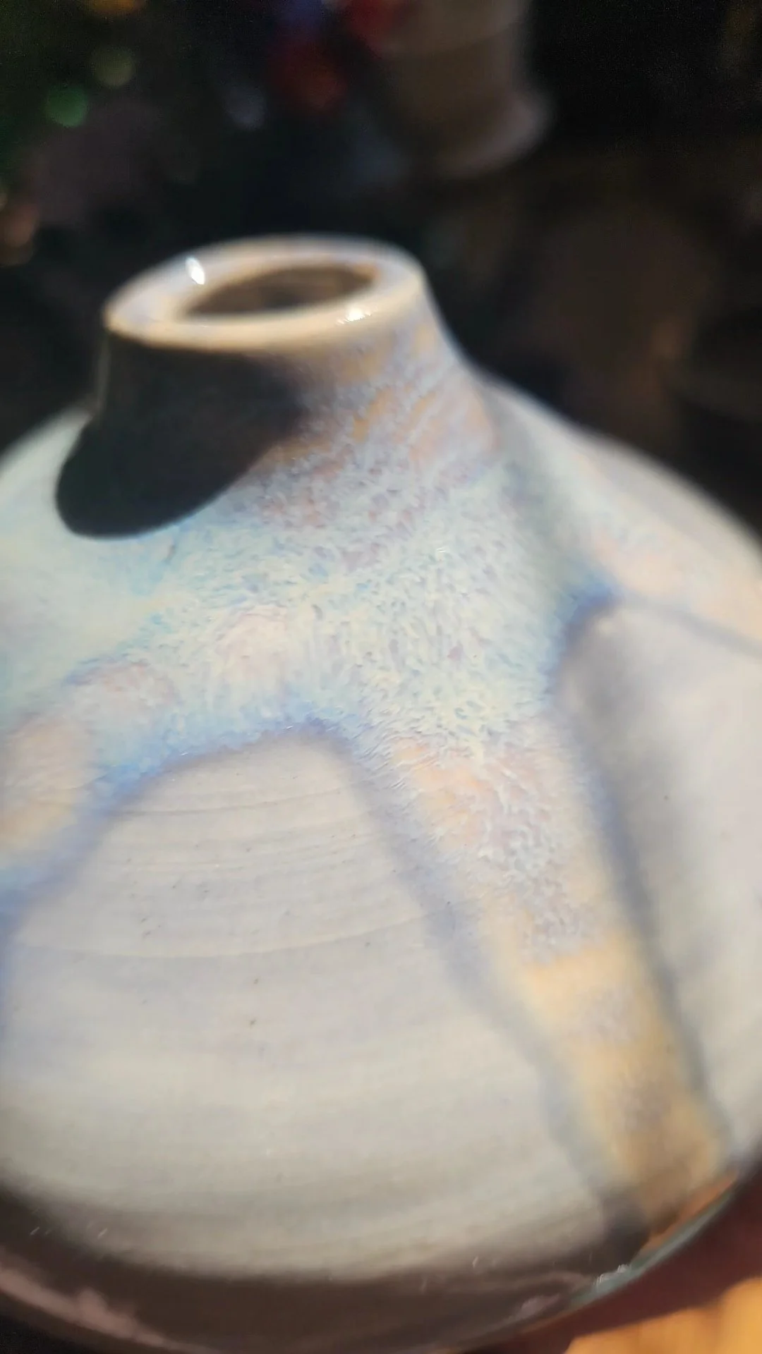 Close-up of a ceramic or porcelain object with a narrow opening, showing a smooth, glazed surface with subtle iridescent streaks.