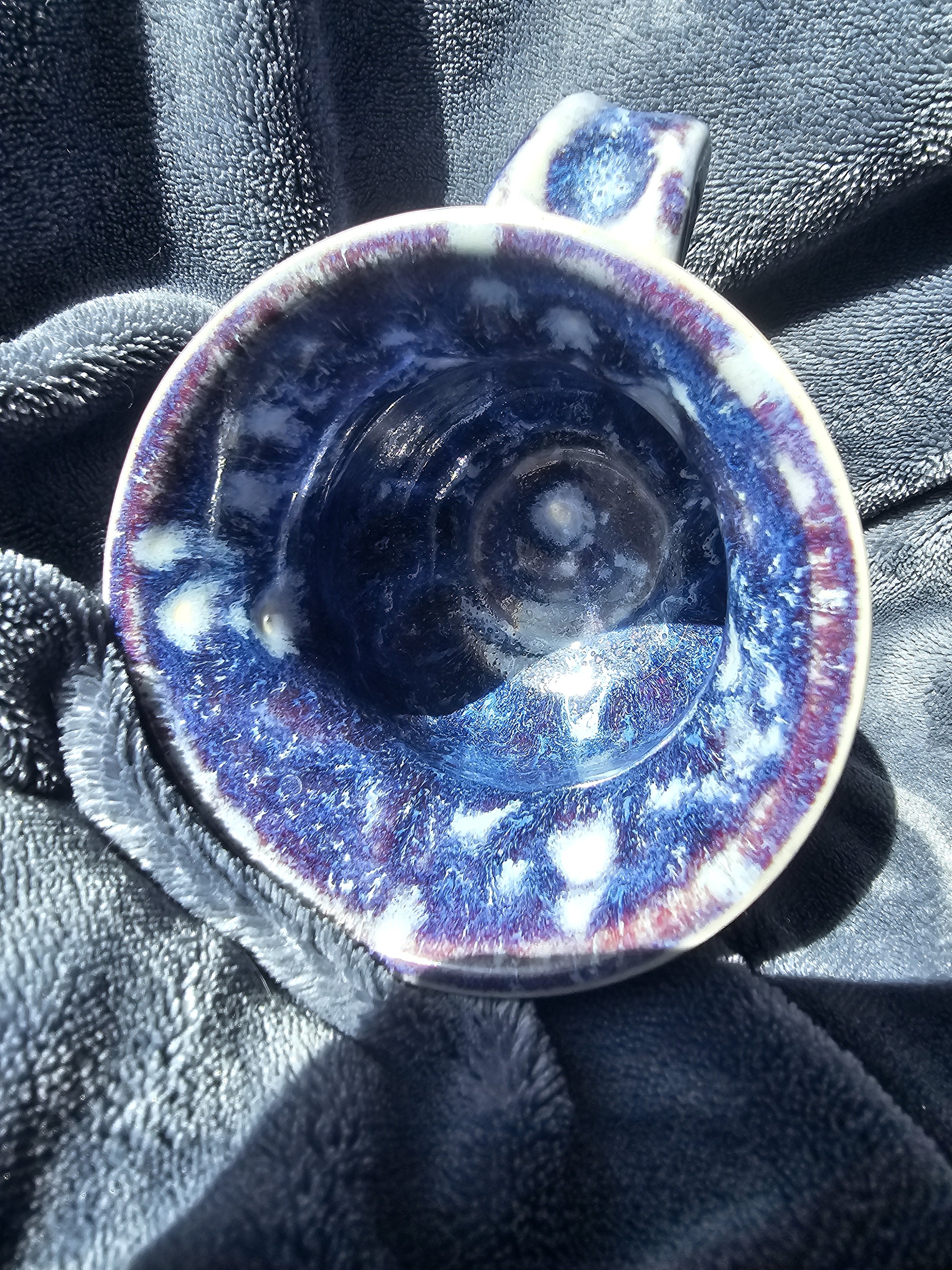 Close-up of a small, colorful ceramic cup with a fiery blue, purple, and white glaze, resting on black.
