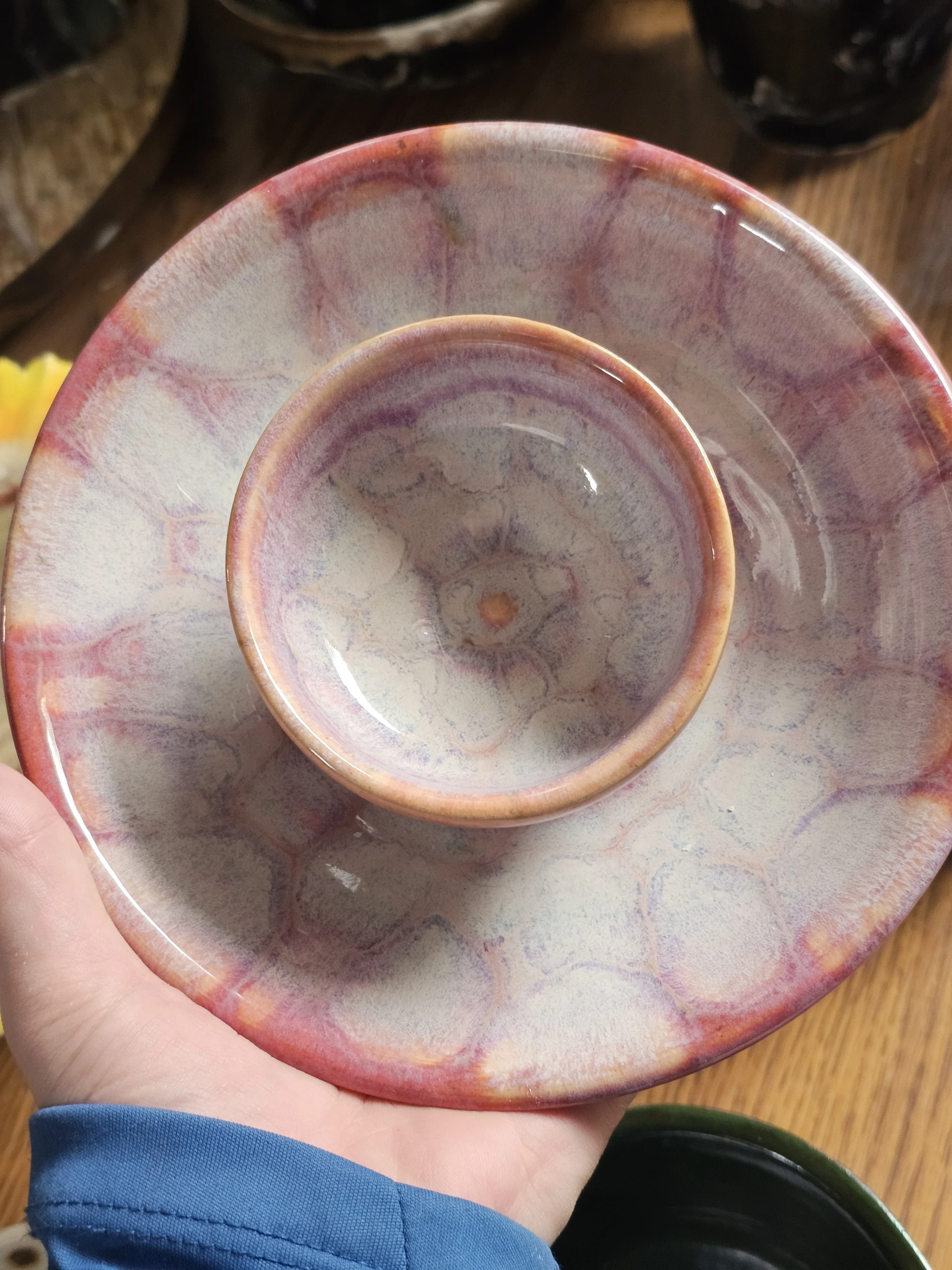 A person holding a multi-colored, layered ceramic bowl with a smaller cup of the same pattern inside, on a wooden surface.