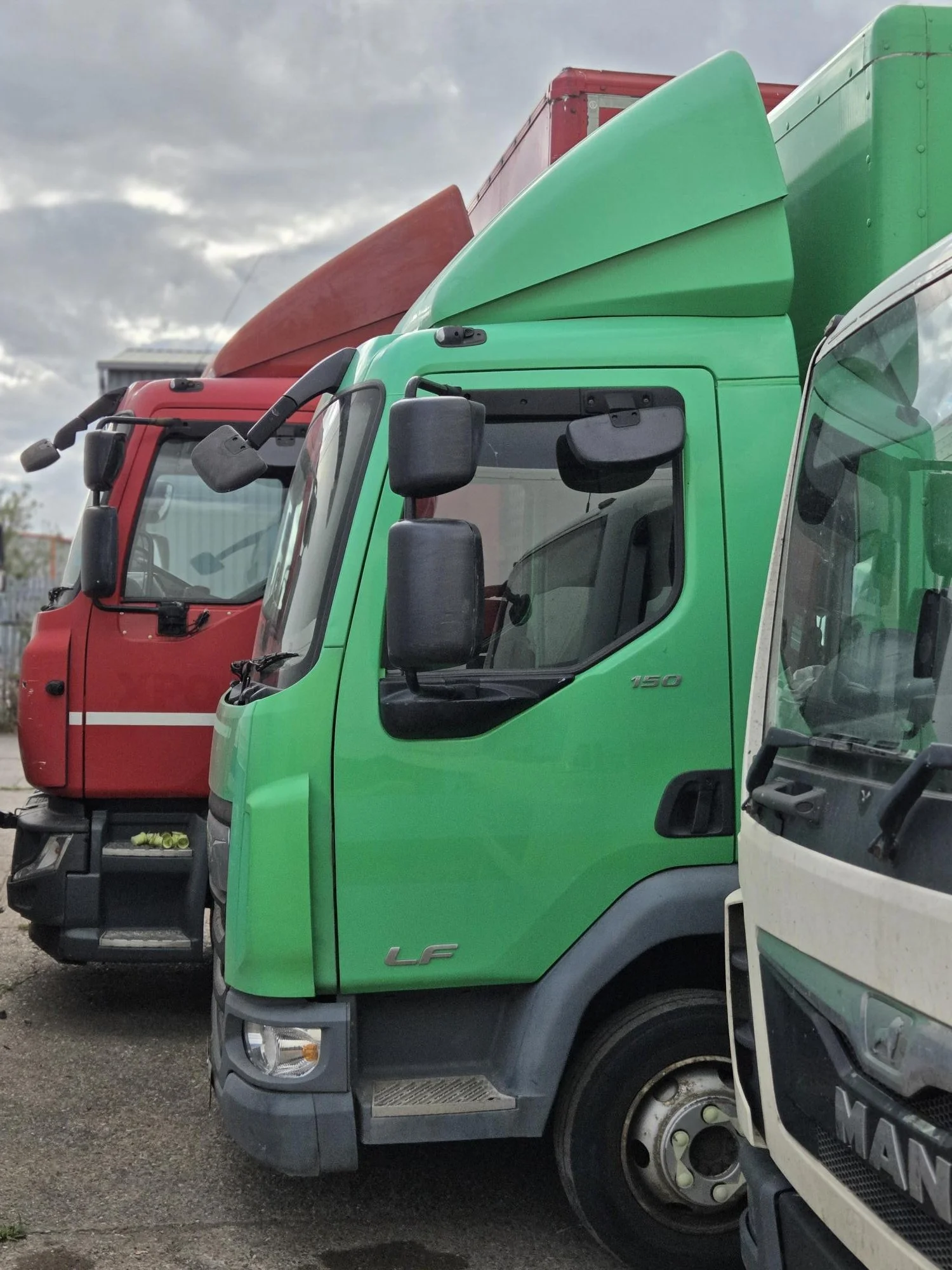 Line of colorful trucks parked side by side, with the focus on a green truck in the foreground.