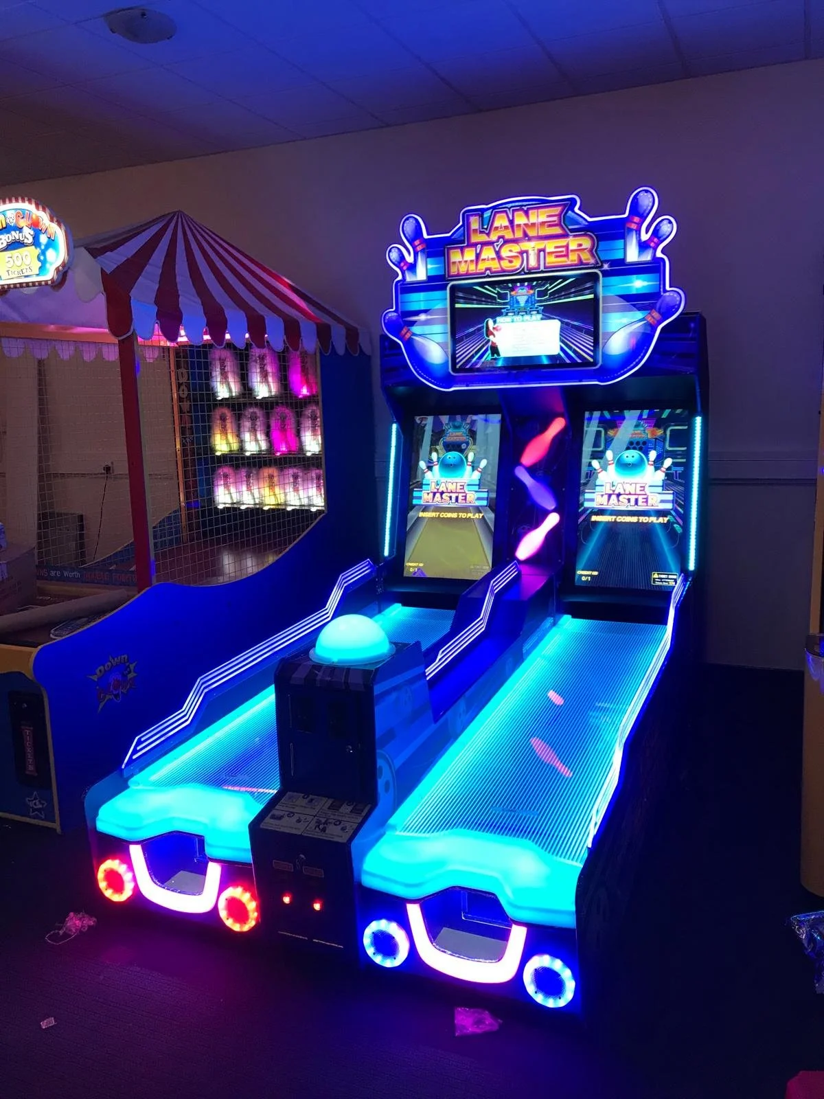 An arcade game called Lane Master with a neon-lit design featuring bowling theme graphics, including bowling pins and a bowling ball, set in an indoor entertainment venue.