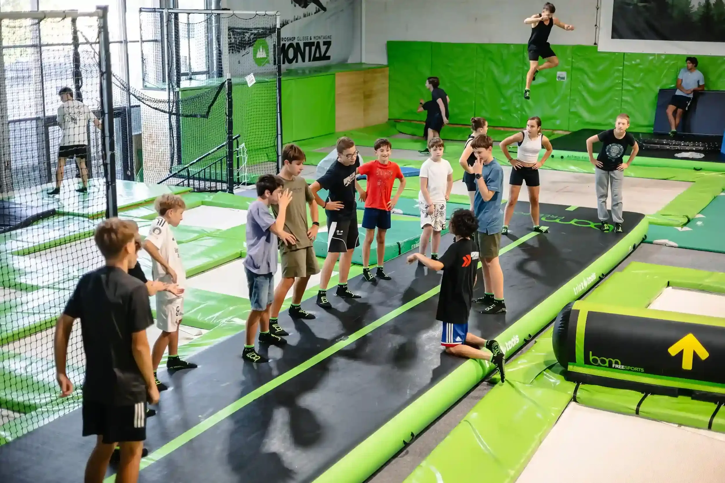 Jeunes pratiquants de trampoline freestyle qui s'échauffent dans la salle de BAM FREESPORTS Chambéry, accompagnés d'un coach.