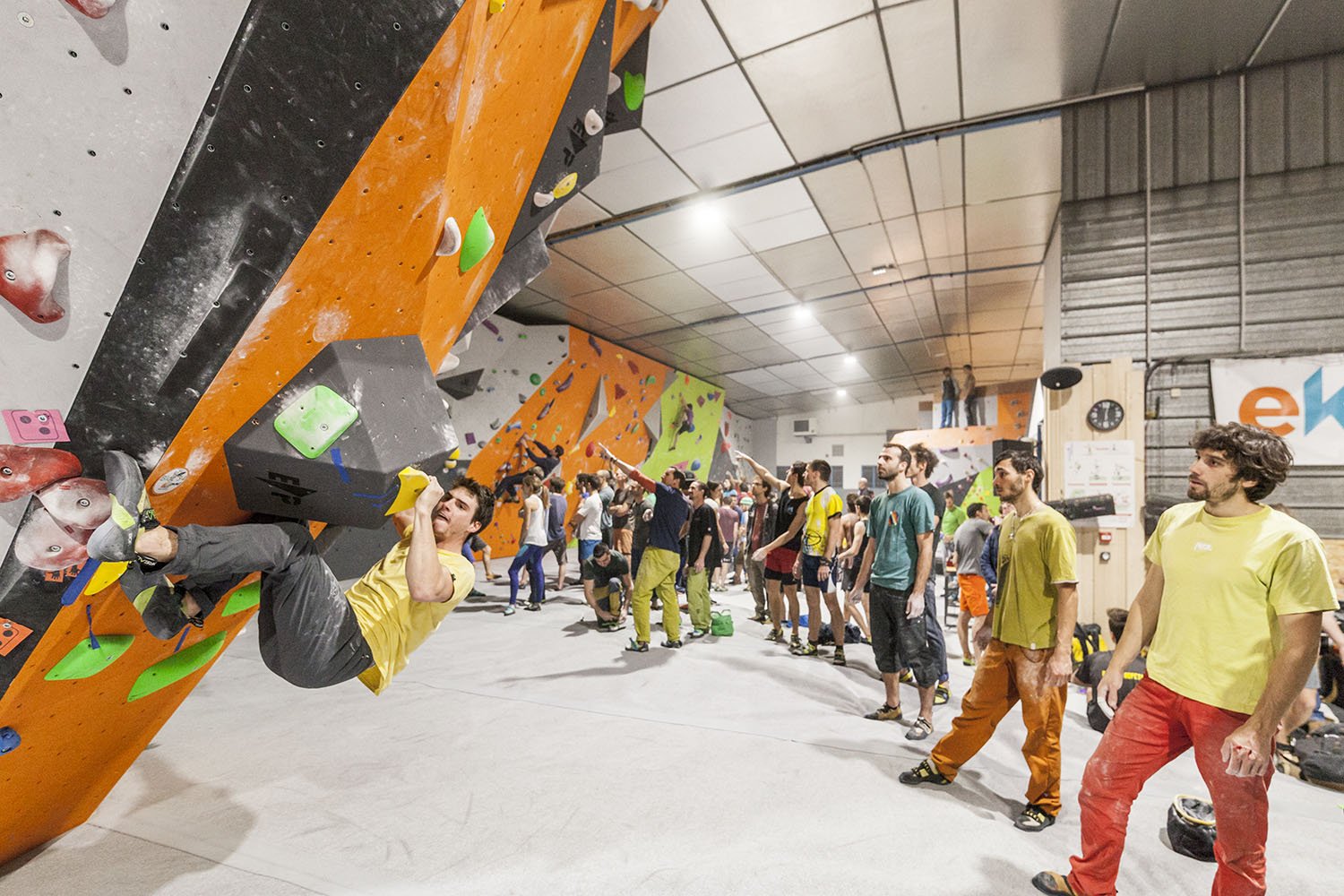 Une salle d'escalade intérieure avec plusieurs grimpeurs, certains en train de grimper et d'autres à attendre.