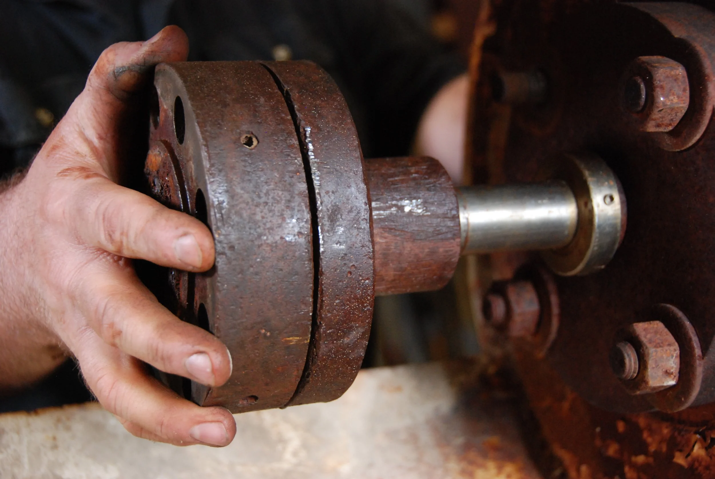 Close-up of a person's hand holding a rusty metal part, possibly a gear or machinery component.