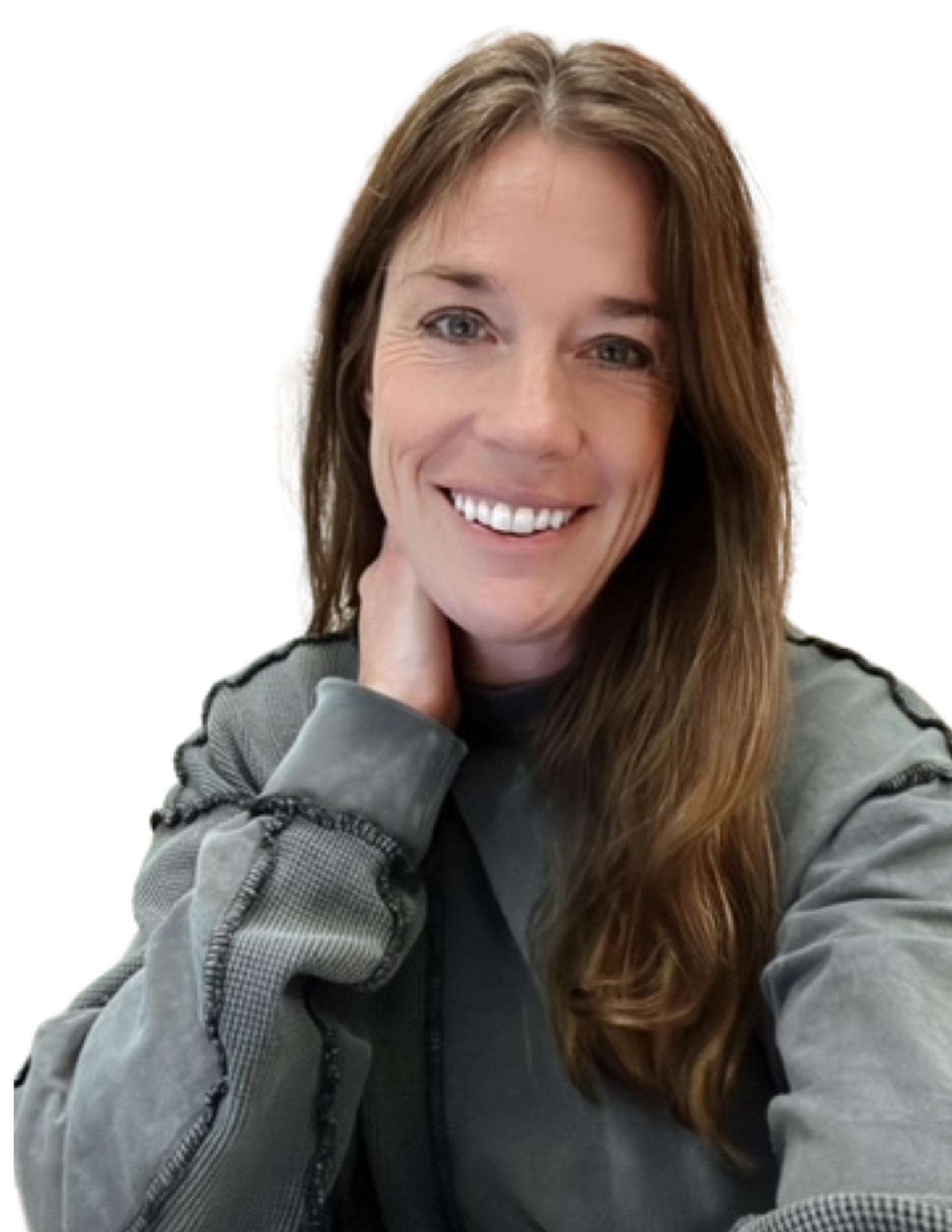 A woman with long brown hair, smiling, wearing a gray jacket over a black shirt, with her hand touching her neck, against a white background.
